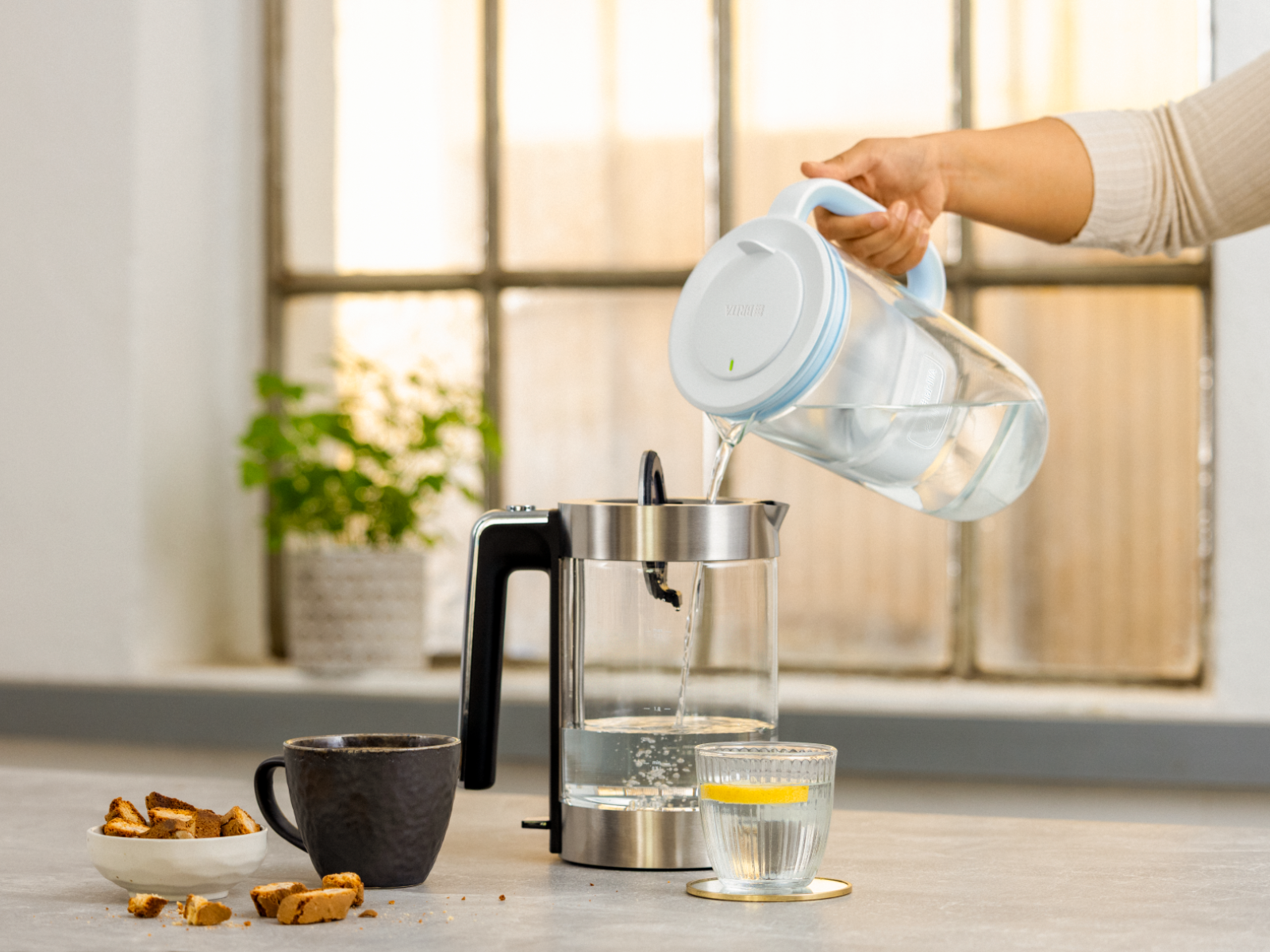 Warum sich Wasser entkalken lohnt Person befüllt mit der BRITA Wasserfilter-Kanne aus Glas einen Wasserkocher