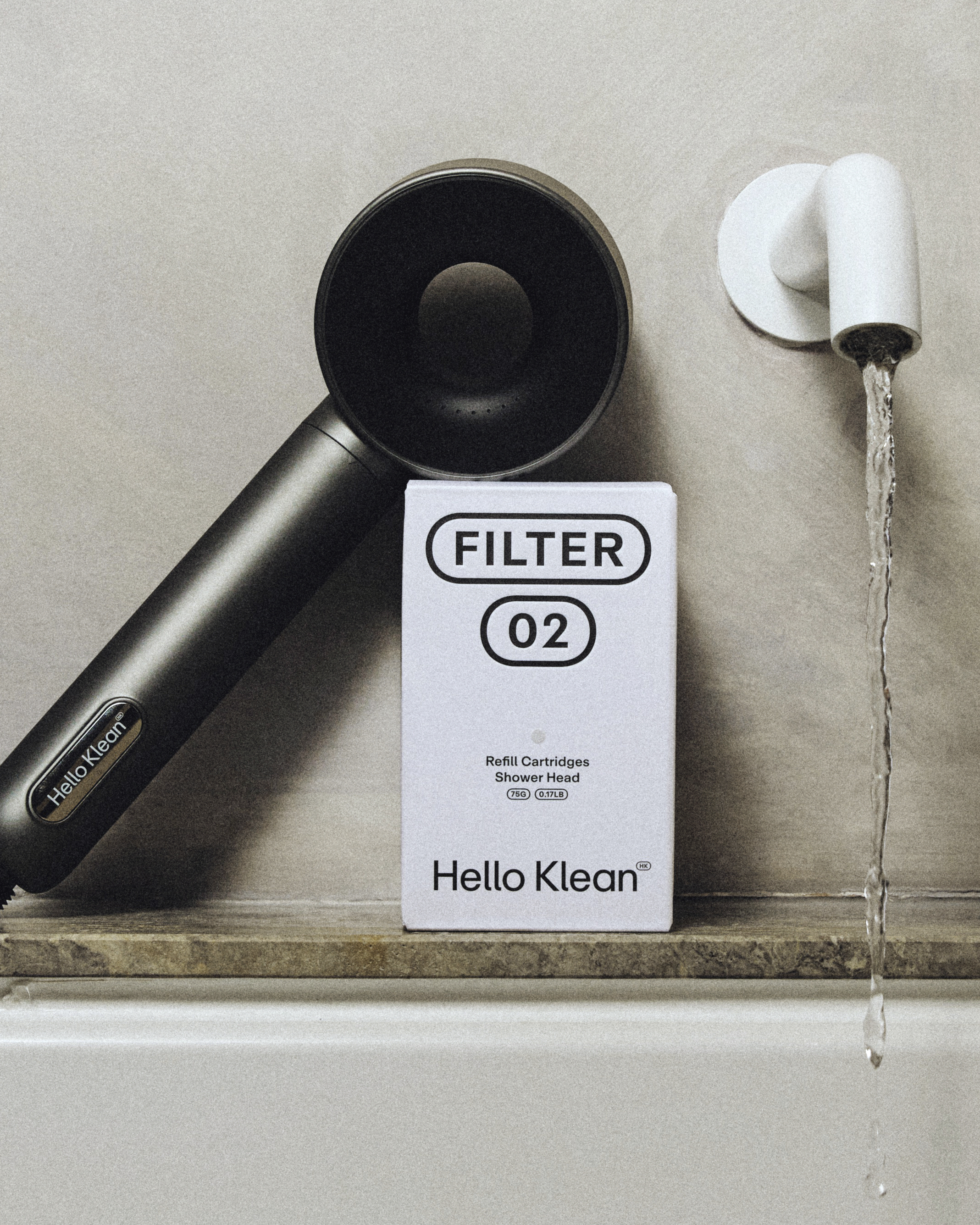 Hello‑Klean‑Duschkopf mit Filter 02 neben der Produktverpackung, Wasser fließt aus der Armatur.

