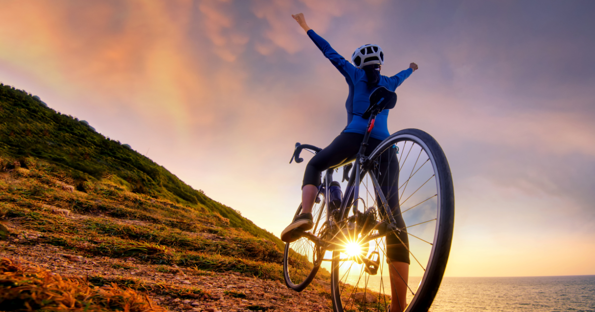 Frau erreicht den Berg bei Sonnenuntergang mit ihrem Fahrrad und fühlt sich lebendig.