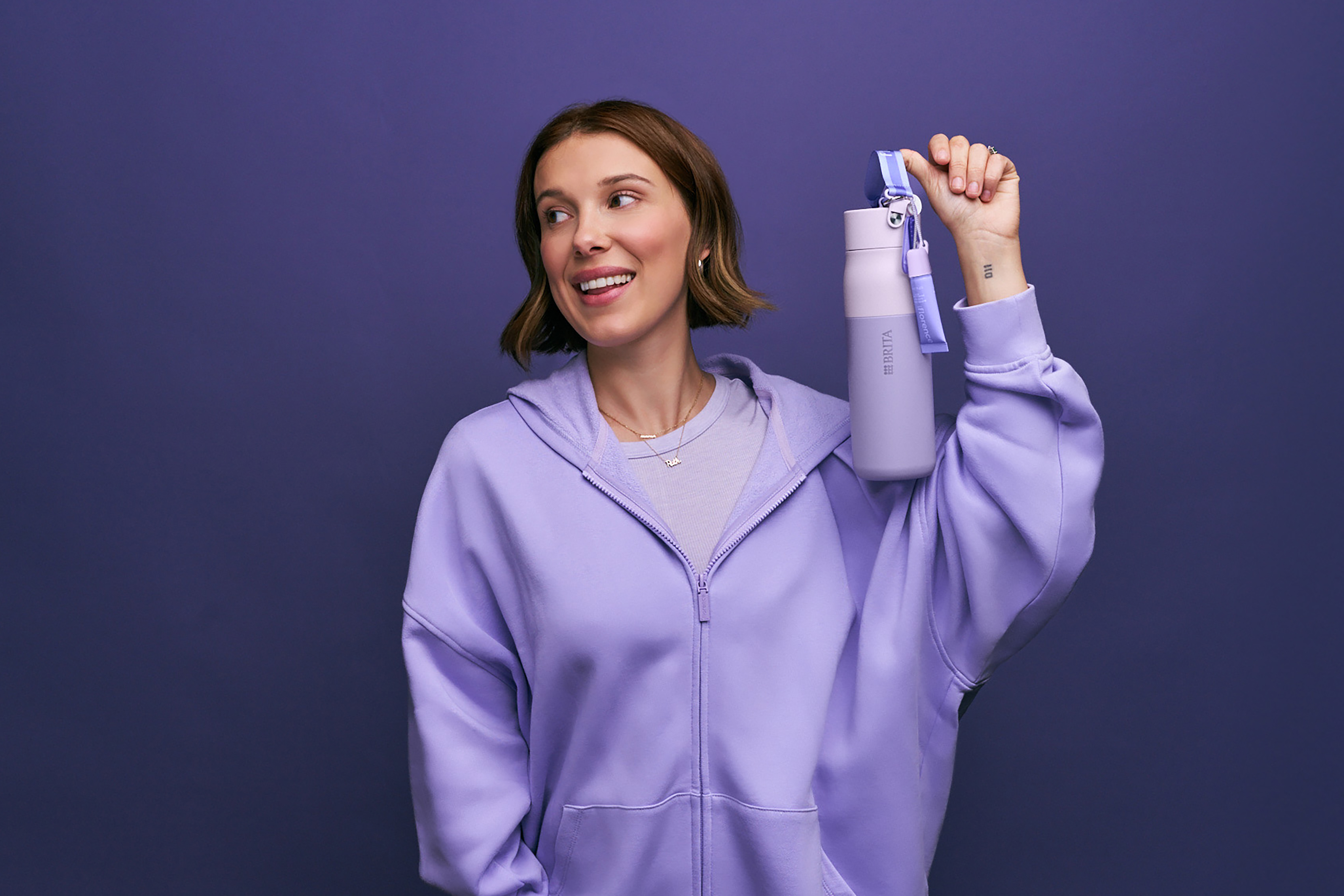 Millie Bobby Brown in lila Sweatshirt hält florence by mills x BRITA LARQ Flasche hoch