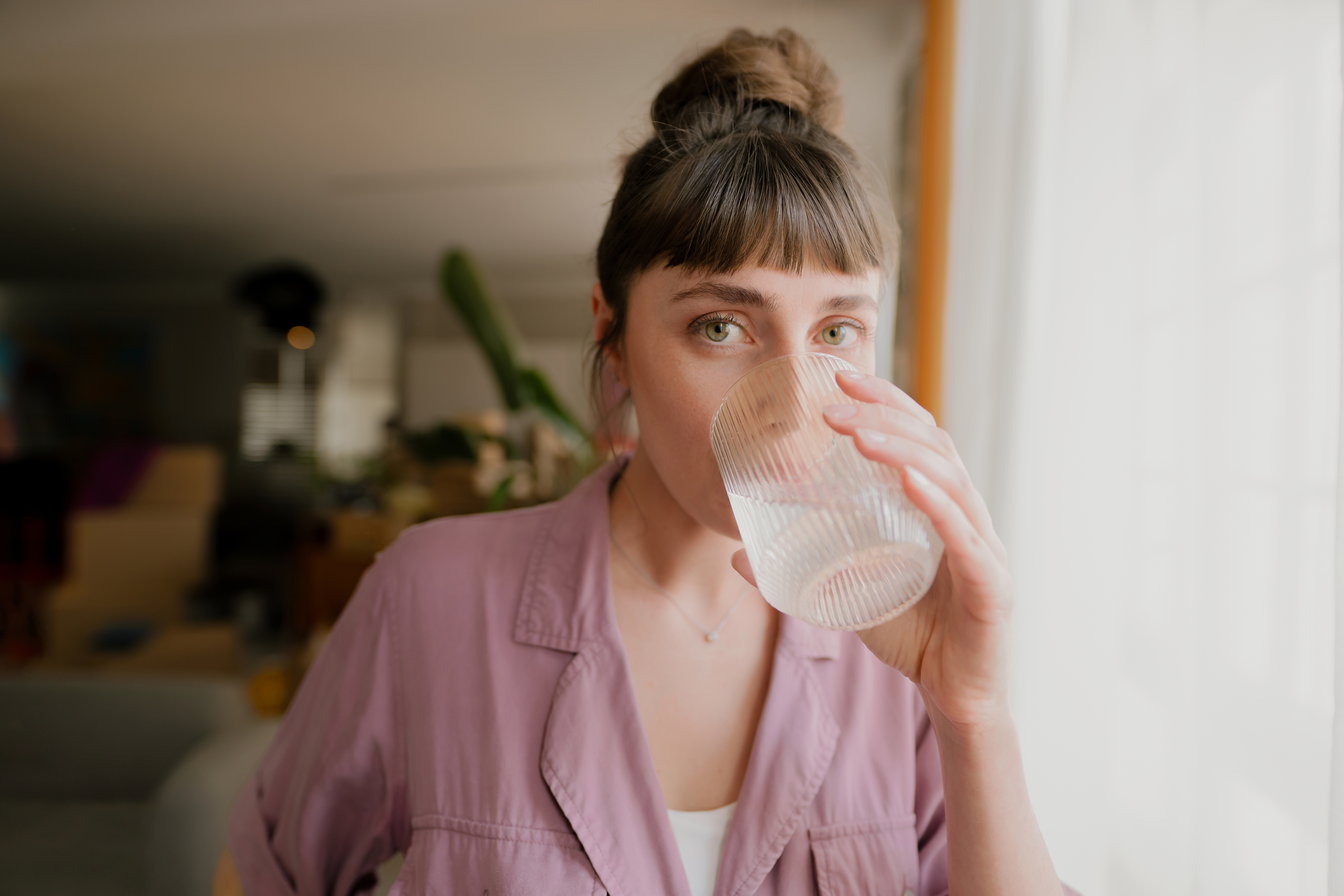 Frau in heller Bluse trinkt Wasser aus einem Glas