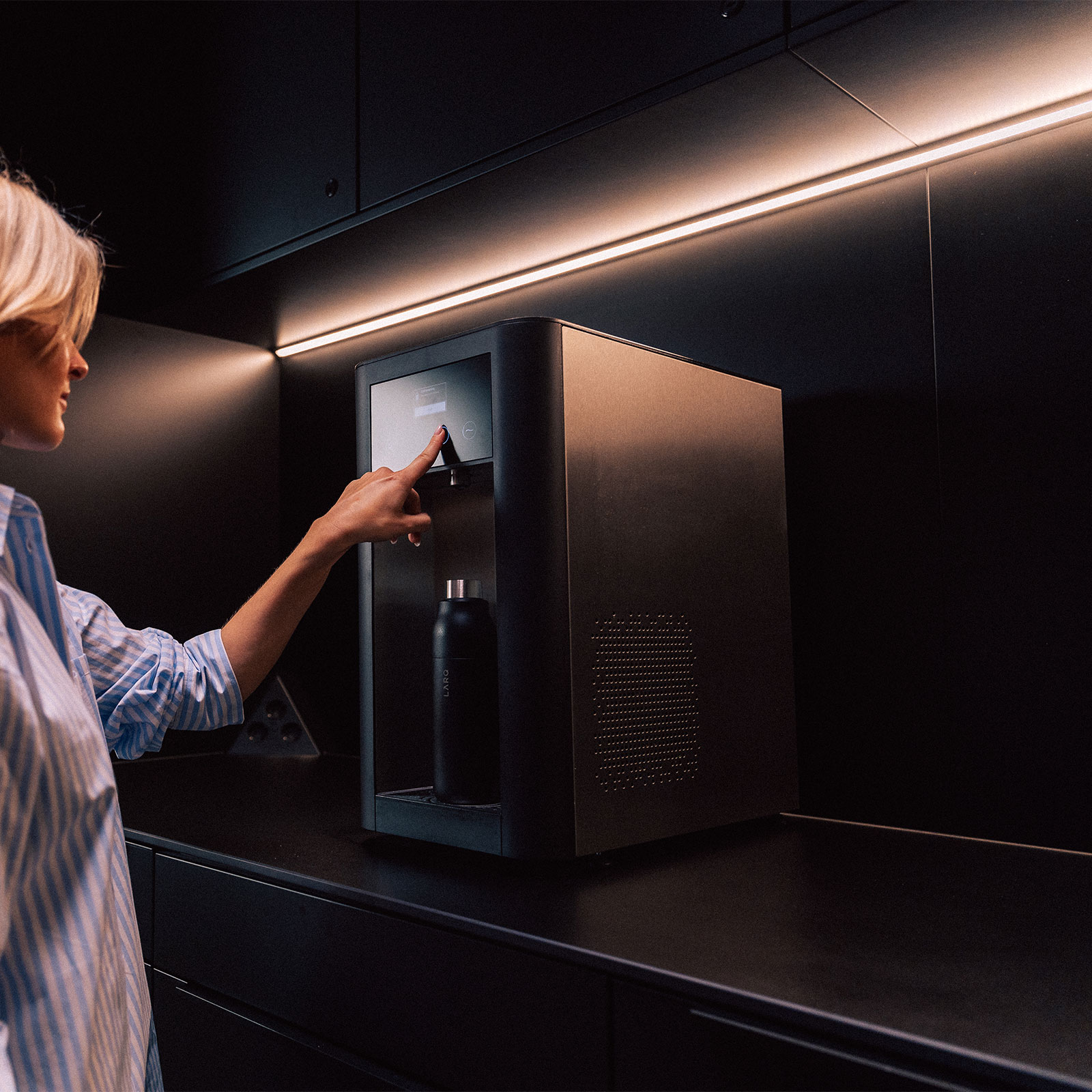 Frau füllt ein Glas Wasser am Dispenser auf Eine blonde Frau benutzt den Wasserspender top pro, um sich ein Glas Wasser einzuschenken.