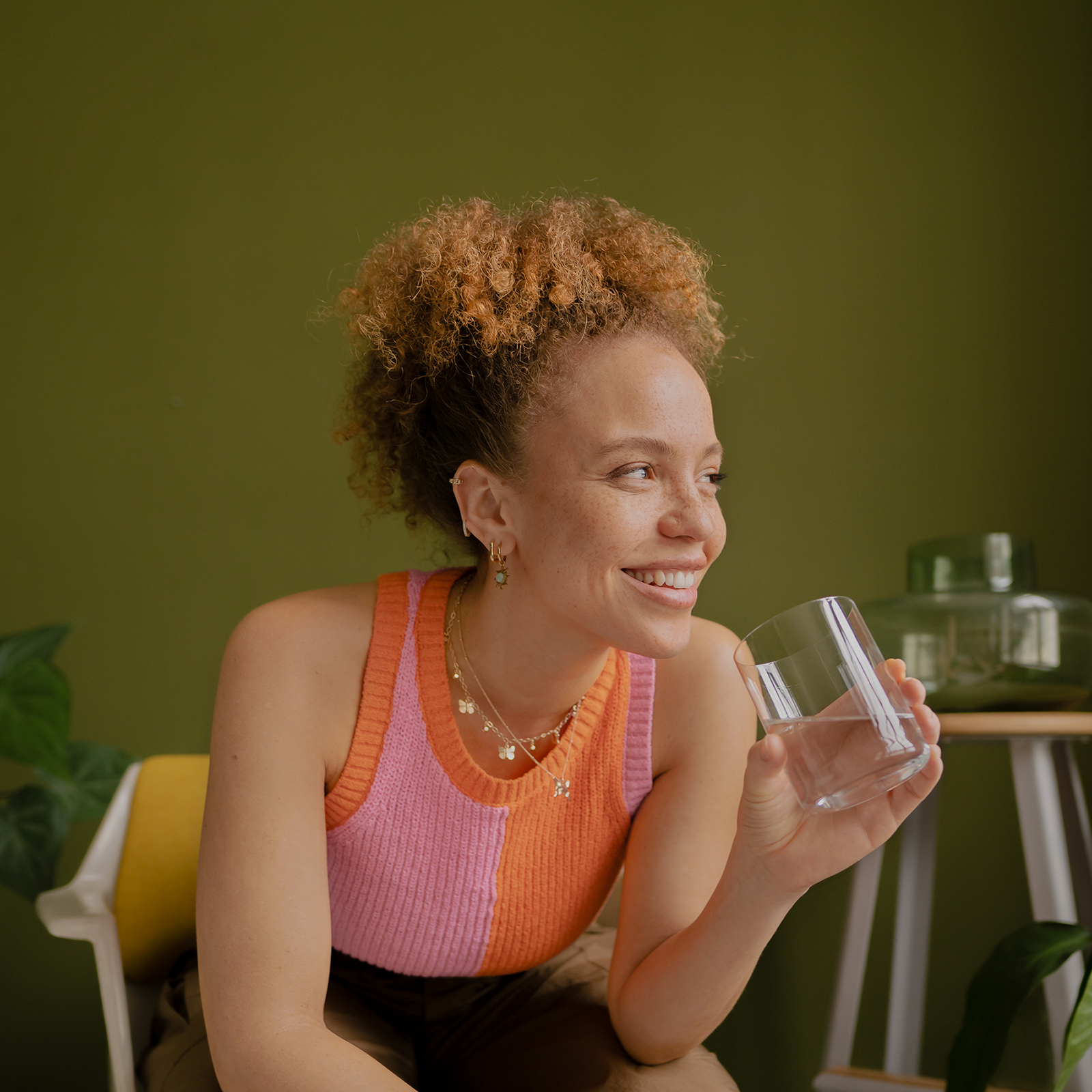 Eine Frau sitzt lächelnd auf einem Stuhl mit einem Glas Wasser in der Hand