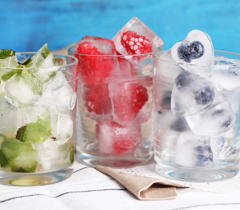 Fruchtige Eiswürfel selber machen Eiswürfel mit Himbeeren, Blaubeeren und Minze in Gläsern für Drinks mit gefiltertem Wasser