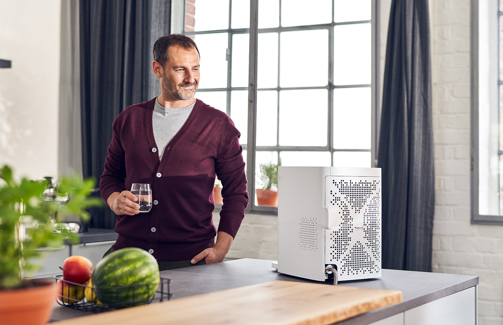 Ein Mann trinkt ein Glas Wasser. Der Wasserspender yource pro top ist mit der Rückseite zu sehen.