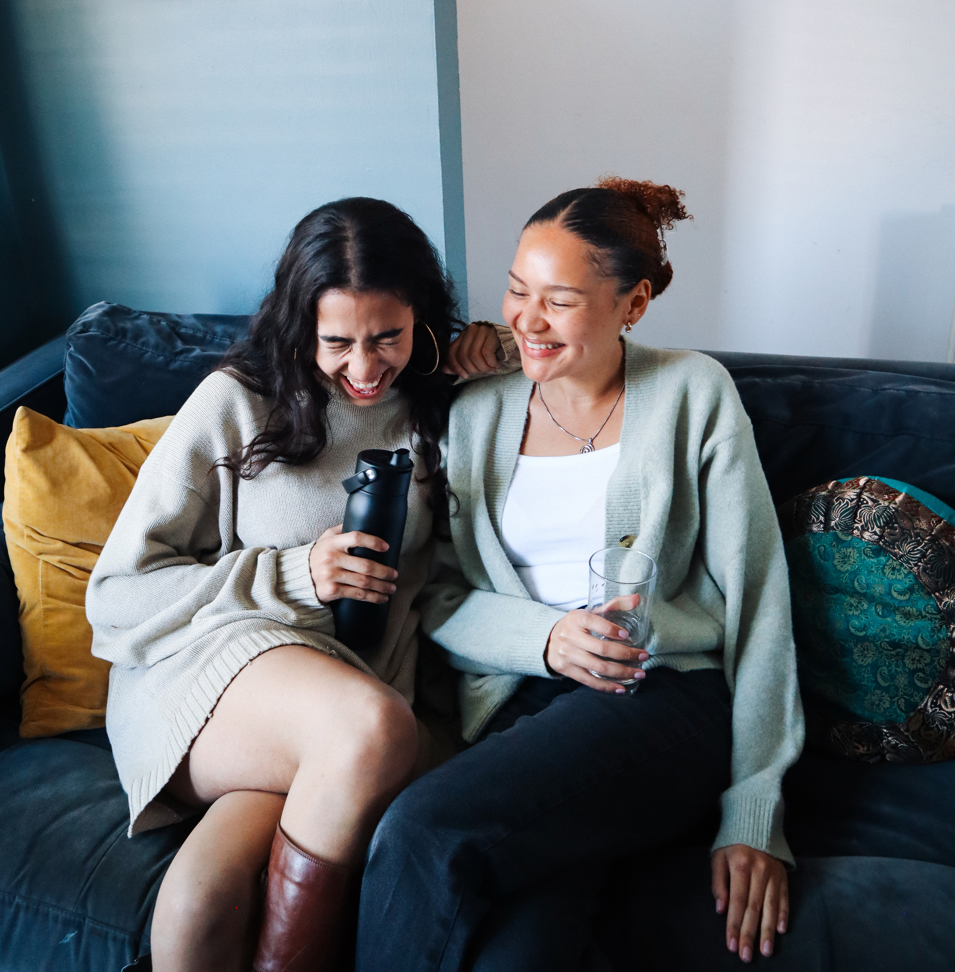Zwei Frauen sitzen lachend mit der BRITA LARQ Flasche auf einer Couch.
