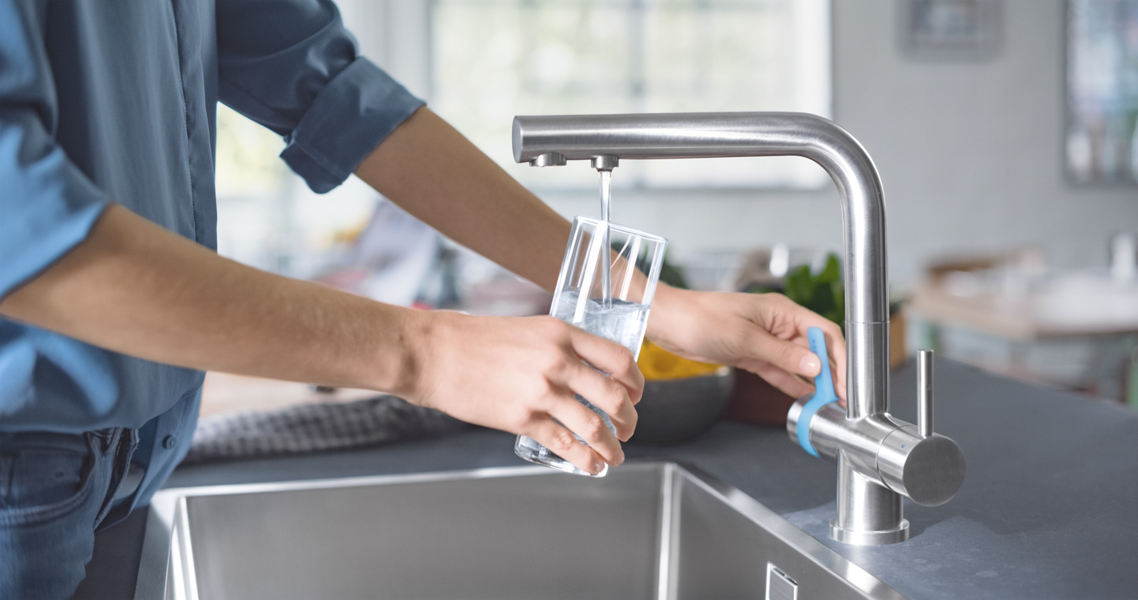 Frau füllt am BRITA 3 Wege Küchenarmatur Glas auf Eine Frau füllt in einer Küche Ihr Wasserglas mit der BRITA 3 Wege Küchenarmatur auf