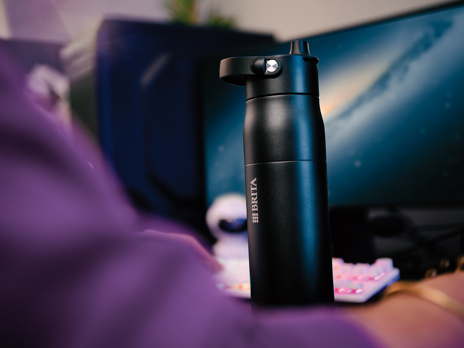 Schwarze BRITA LARQ iQ Flasche steht neben Monitor auf Schreibtisch.
