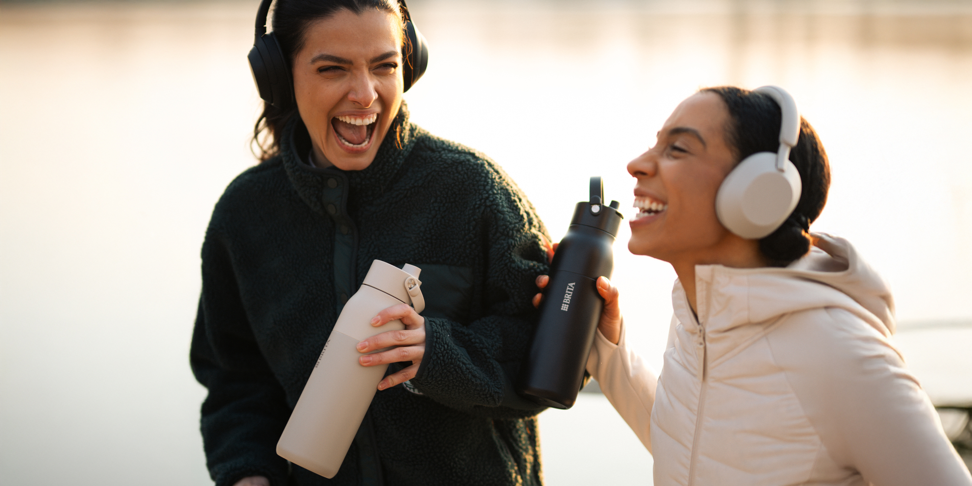 Zwei junge Frauen beim Joggen mit BRITA LARQ Flasche Zwei junge Frau trinken während sie joggen Wasser mit der BRITA LARQ Filterflasche