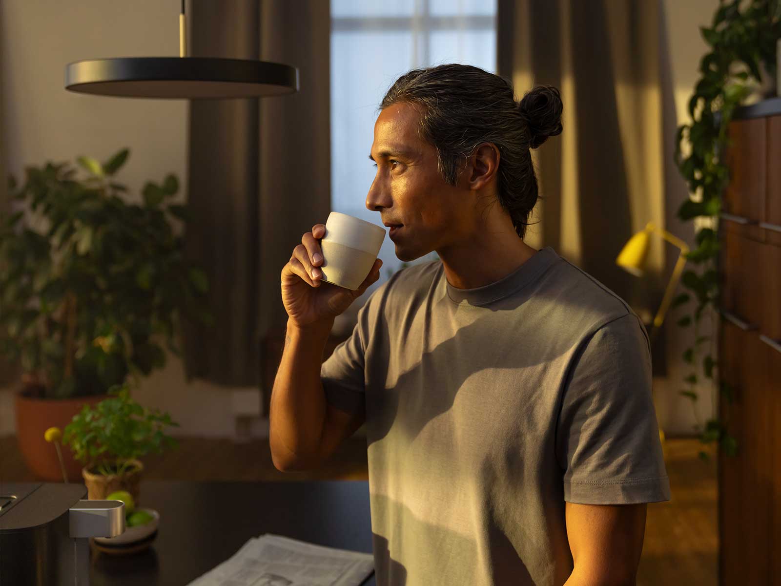 Mann trinkt aus Tasse Ein dunkelhaariger Mann in einem beigen Shirt trinkt aus einer Tasse.