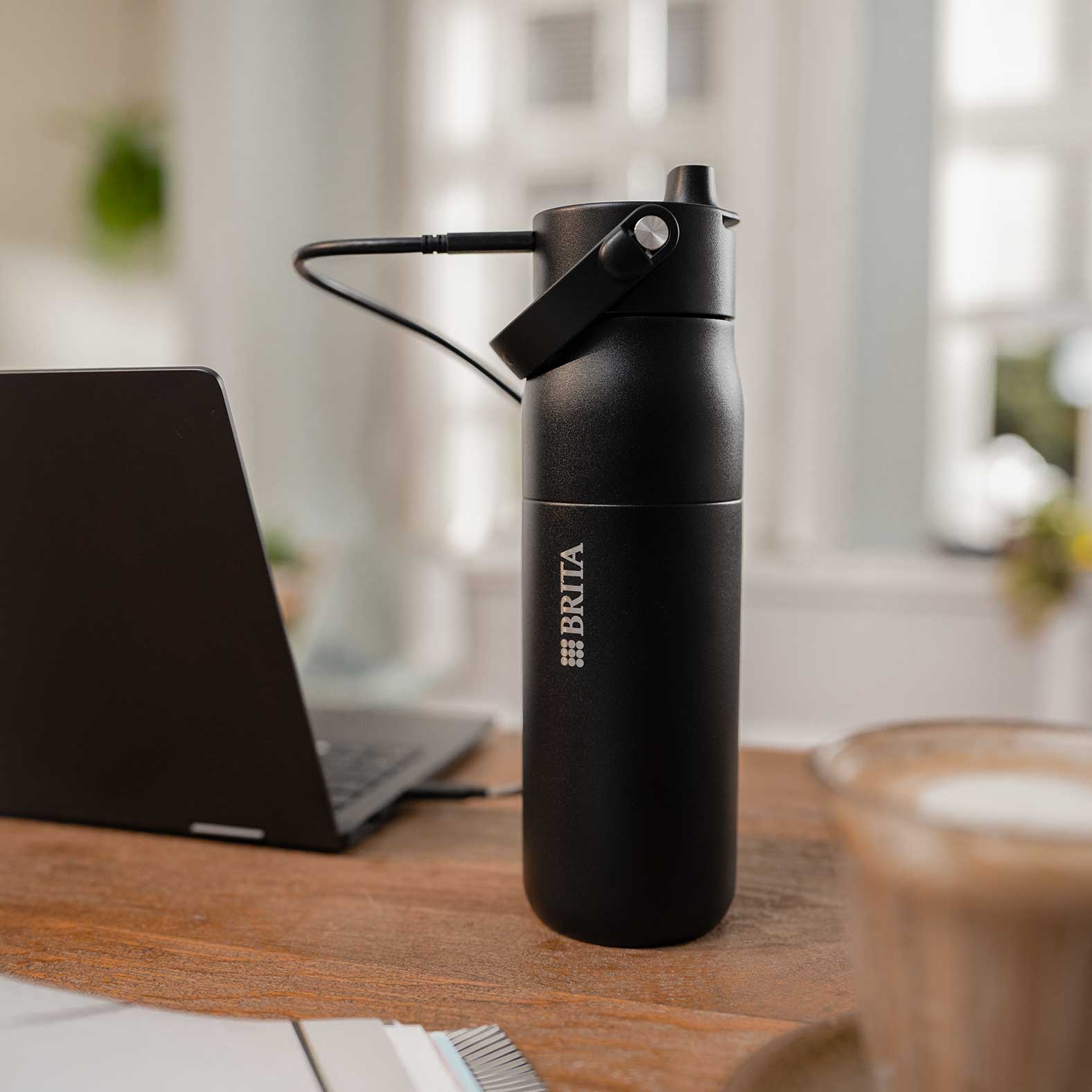 Die BRITA LARQ iQ im Homeoffice – immer einsatzbereit Eine schwarze BRITA LARQ iQ Filterflasche wird auf einem Schreibtisch per Kabel geladen