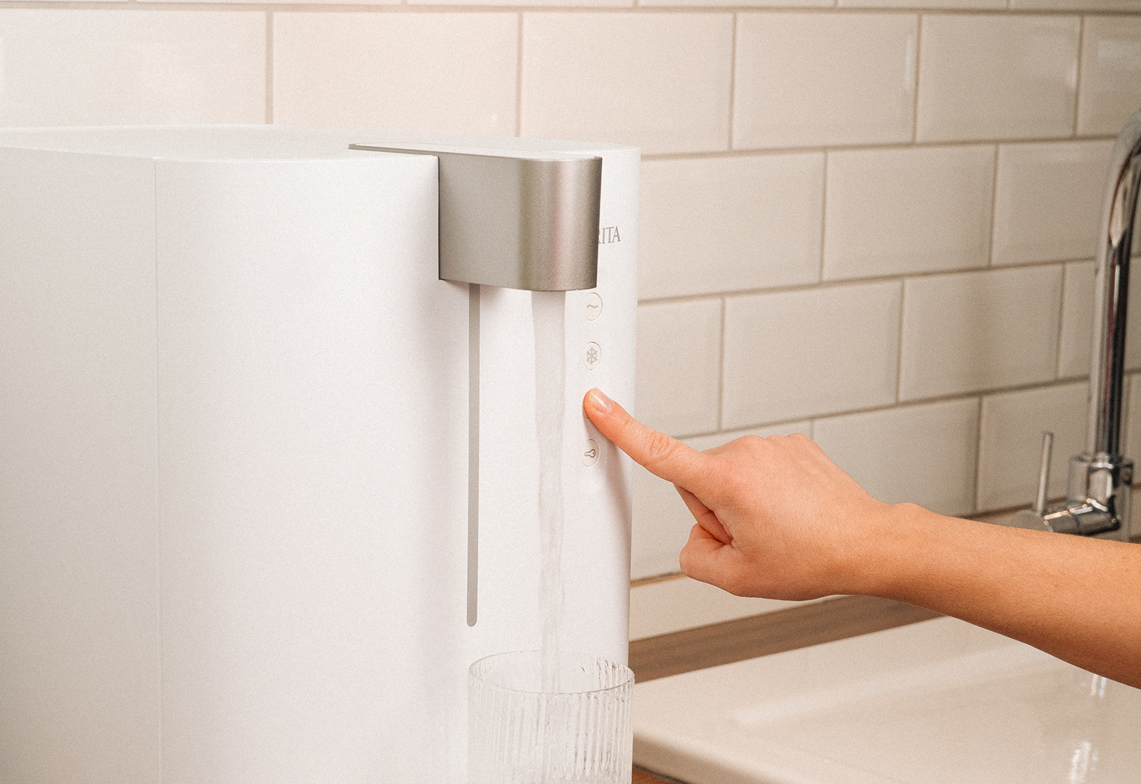 Wasser auf Knopfdruck mit BRITA yource pro top Frau drückt Taste am BRITA yource pro top, während ein Glas mit frischem Wasser befüllt wird