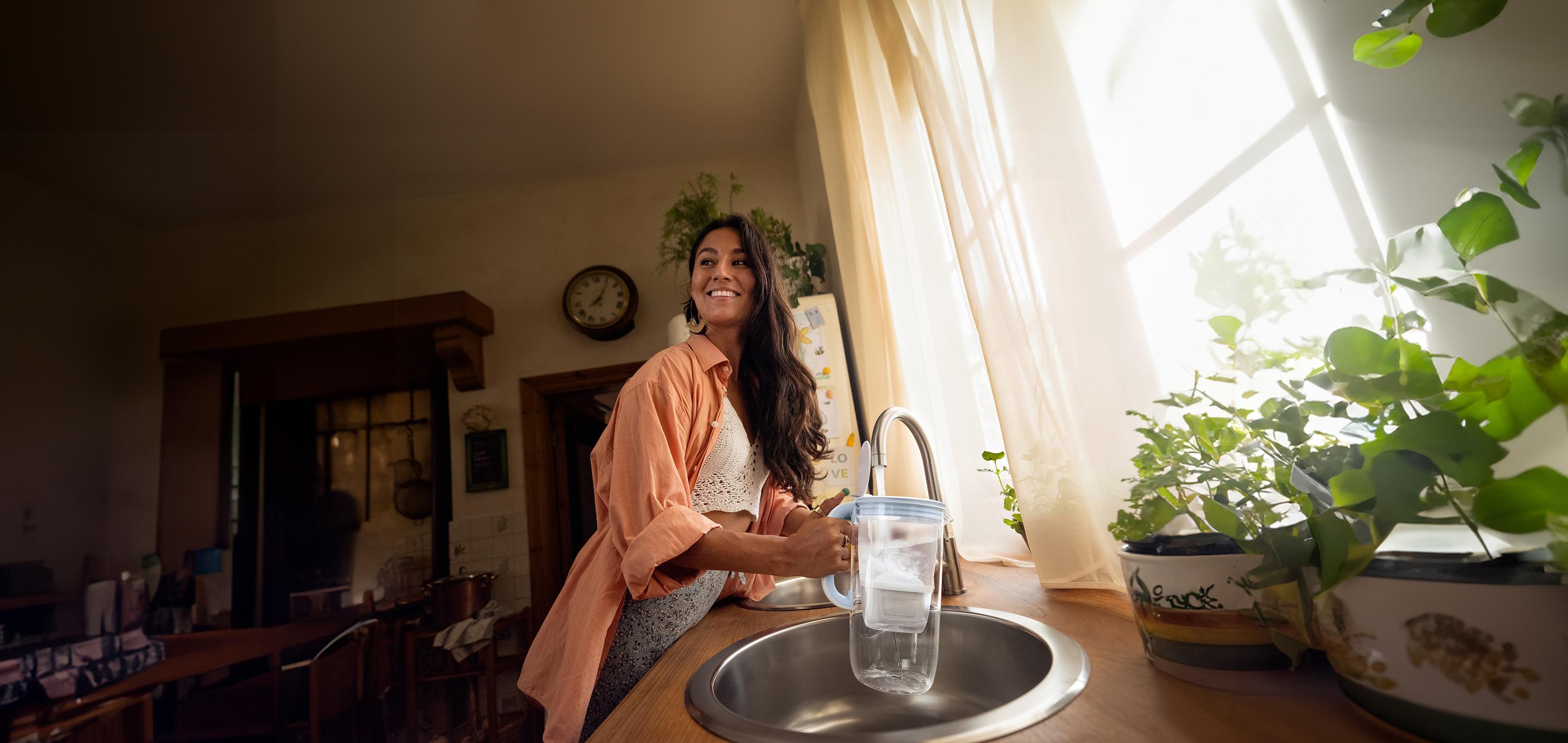 Eine junge Frau filtert Leitungswasser mit dem Tischwasserfilter BRITA Glas
