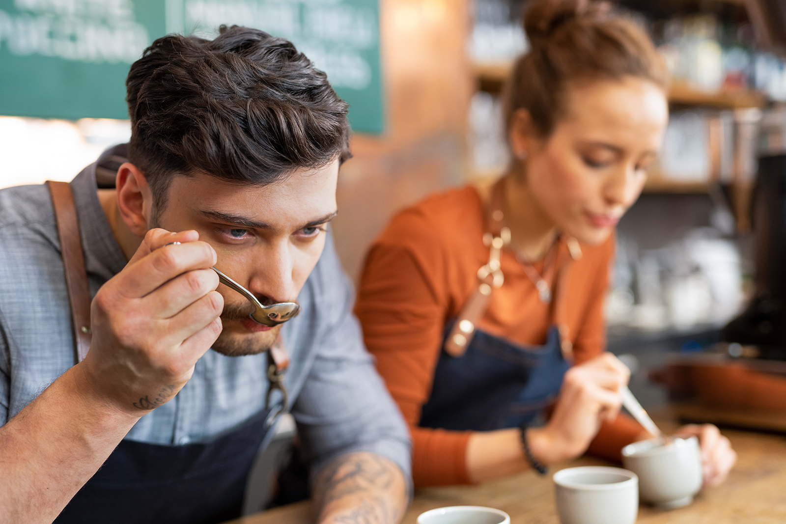 Mann und Frau bei einer Kaffee-Verkostung Ein Mann und eine Frau verkosten Kaffee mit einem Löffel in einem Café