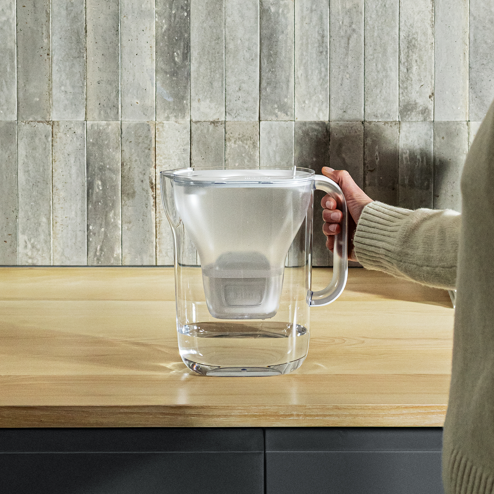 Frau hält den BRITA Style Essential in der Küche fest und der Tischwasserfilter ist gefüllt
