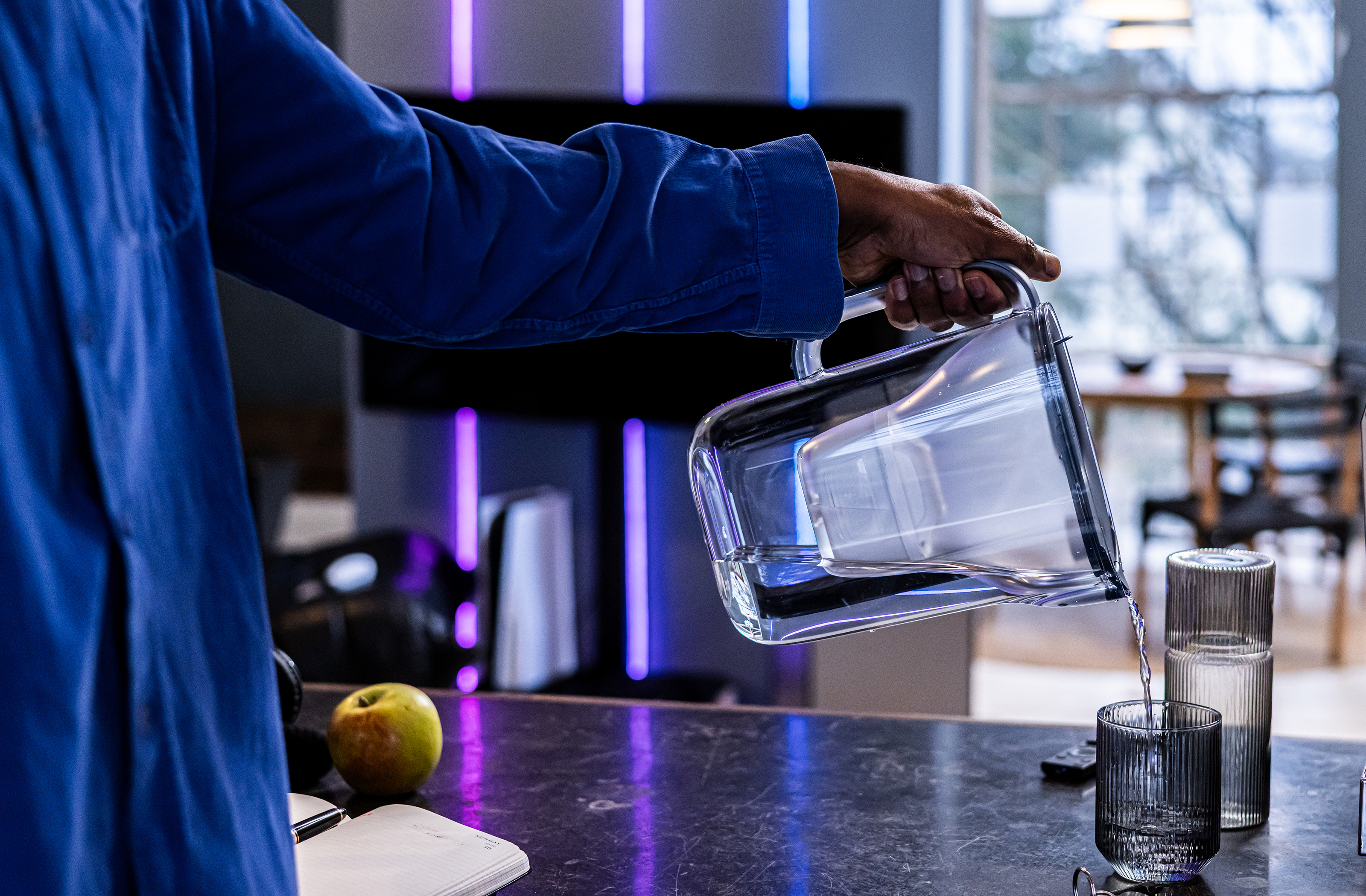 Blauer Tischwasserfilter Style Essential mit Wasserglas Wasser wird aus dem blauen Tischwasserfilter Style Essential in ein Glas geschüttet