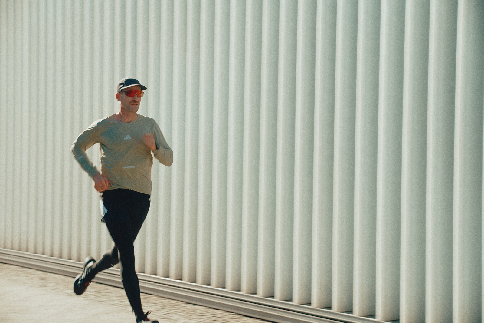 Läufer in Sportkleidung joggt entlang einer hellen, strukturierten Wand in urbaner Umgebung bei Tage