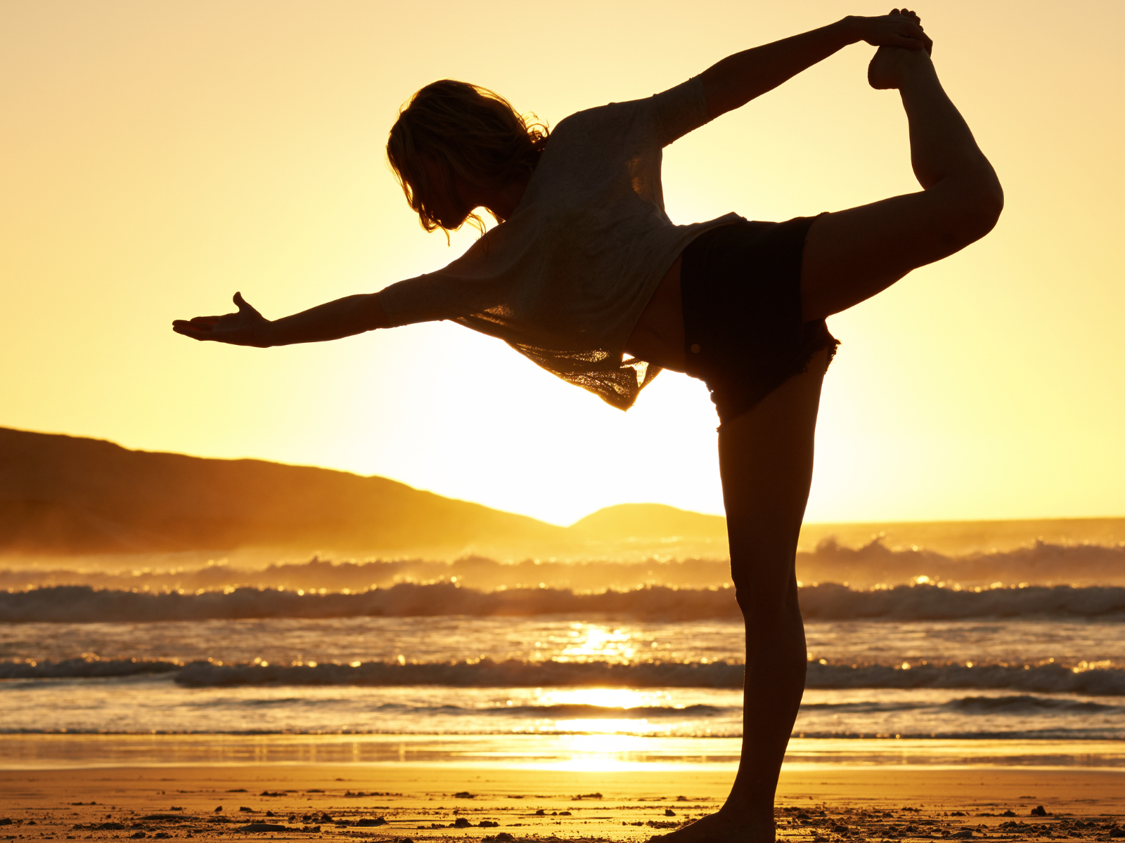 Was bedeutet Achtsamkeit? Frau macht Yoga am Strand bei Sonnenaufgang. Fokussiert auf das Hier und Jetzt.