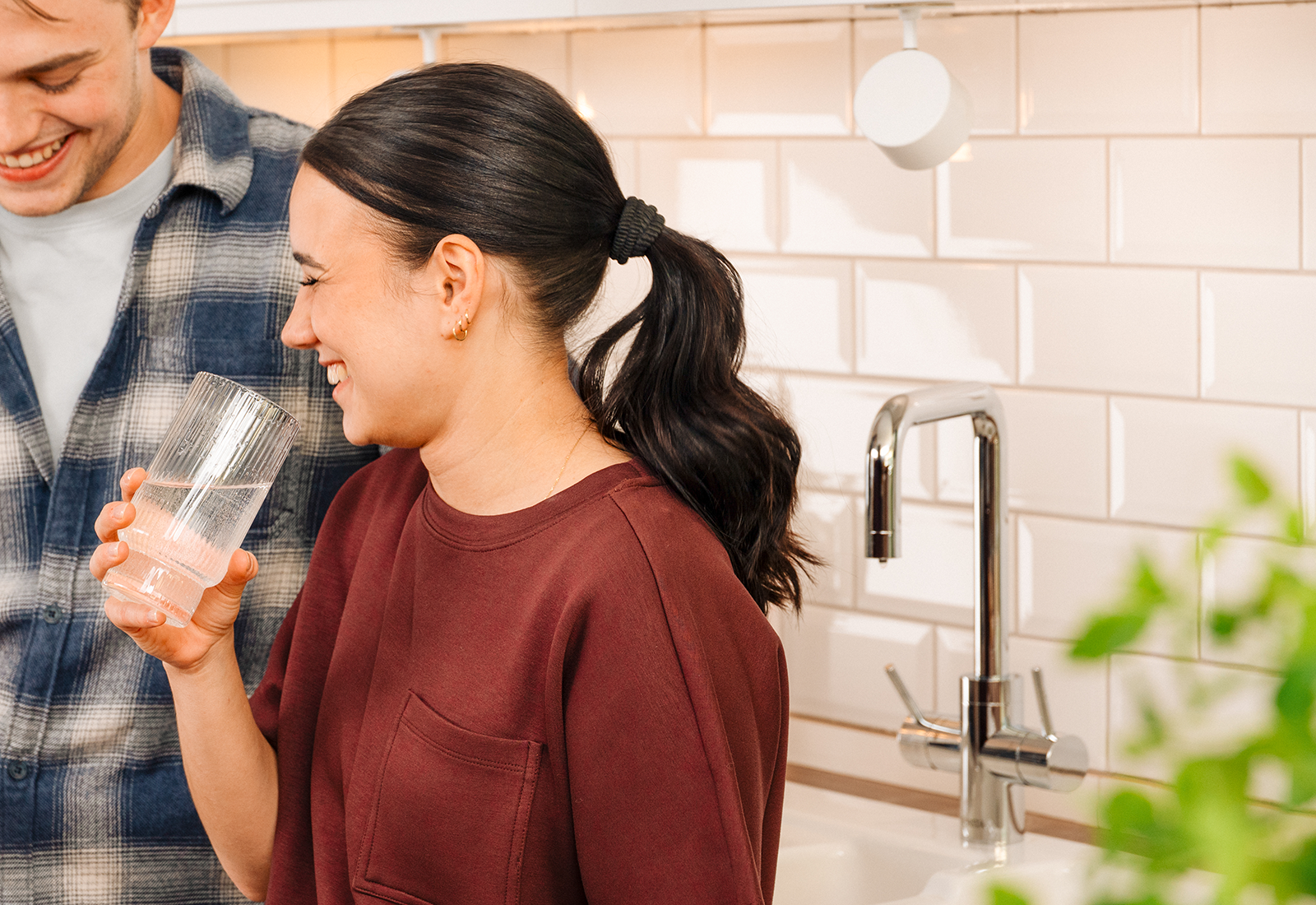 Gemeinsamer Moment in der Küche mit frischem Wasser Zwei Personen in einer modernen Küche, eine hält ein Glas Wasser, die andere ein Smartphone