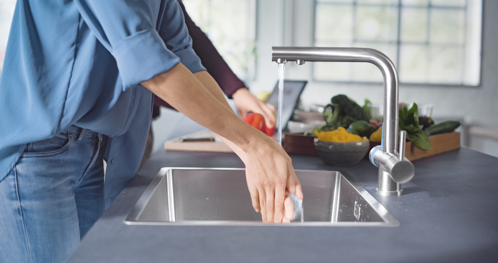 Eine Frau wäschst sich in einer Küche an der BRITA 3 Wege Küchenarmatur die Hände