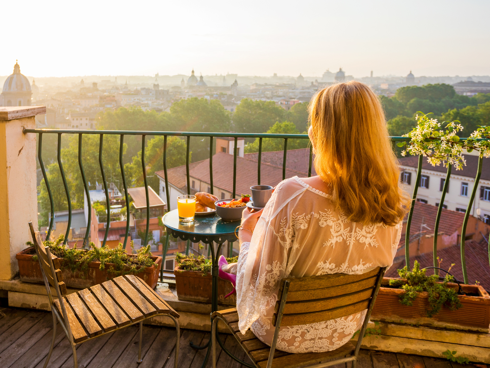 Frau sitzt beim Frühstück auf dem Balkon und genießt den Sonnenaufgang und die Morgenruhe.