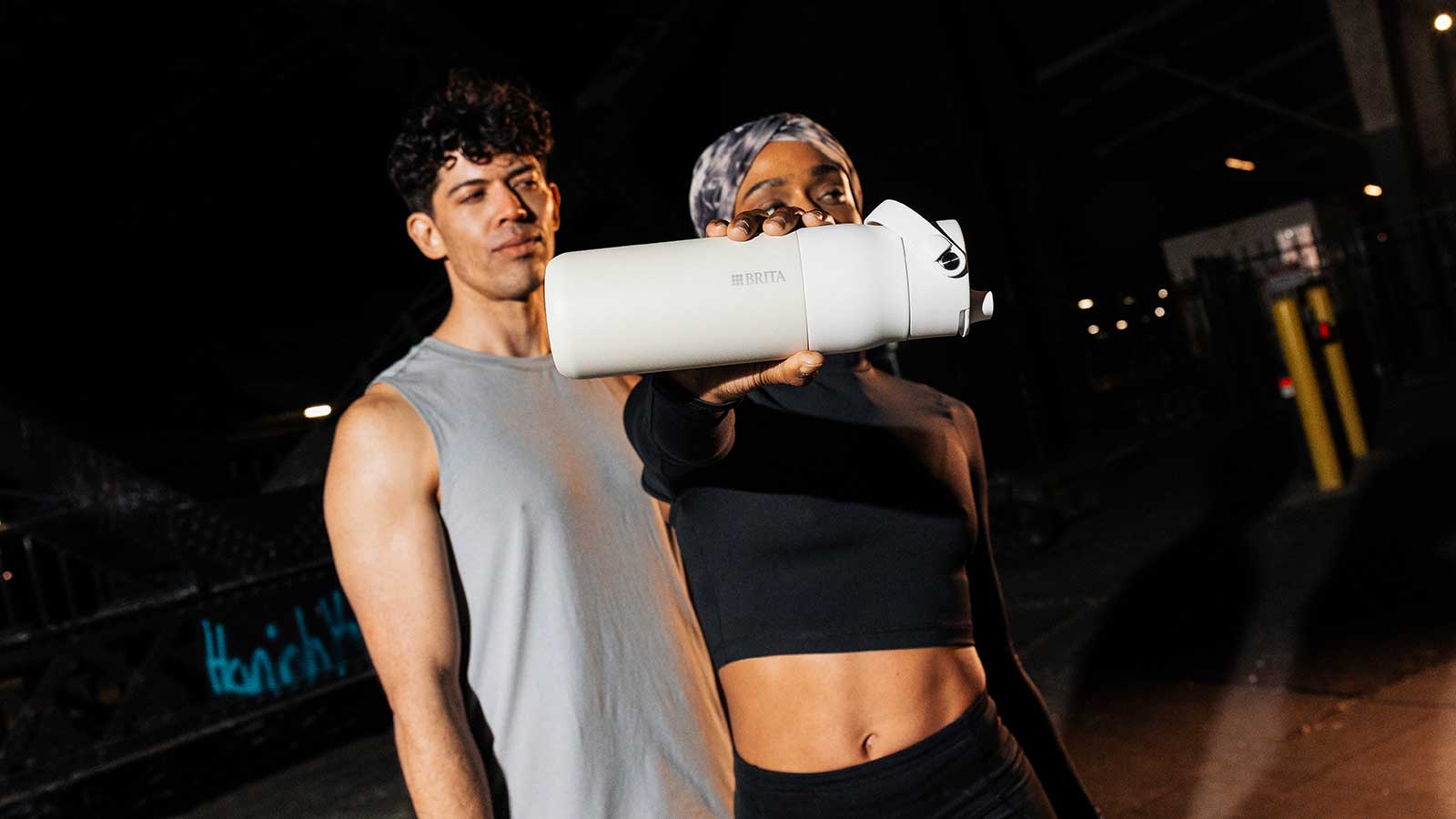 Zwei sportliche Personen posieren im urbanen Setting, eine hält eine weiße BRITA LARQ Filterflasche