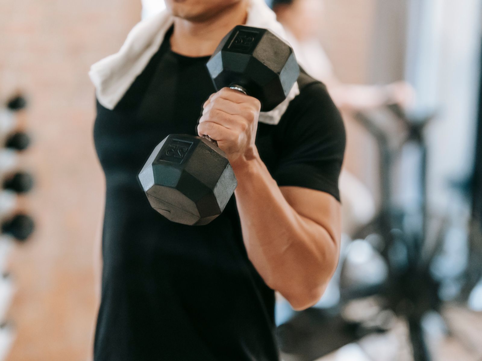 Mann trainiert seinen Arm mit einer Hantel Mann in schwarzem T-Shirt trainiert seinen Arm mit einer Hantel