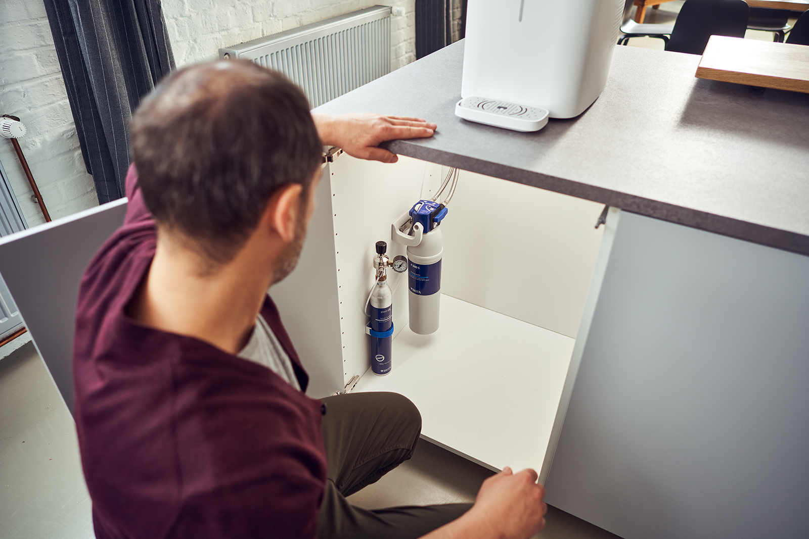 Ein Mann schaut in den Unterschrank einer Küche auf einen CO2 Zylinder und eine Filterkartusche.