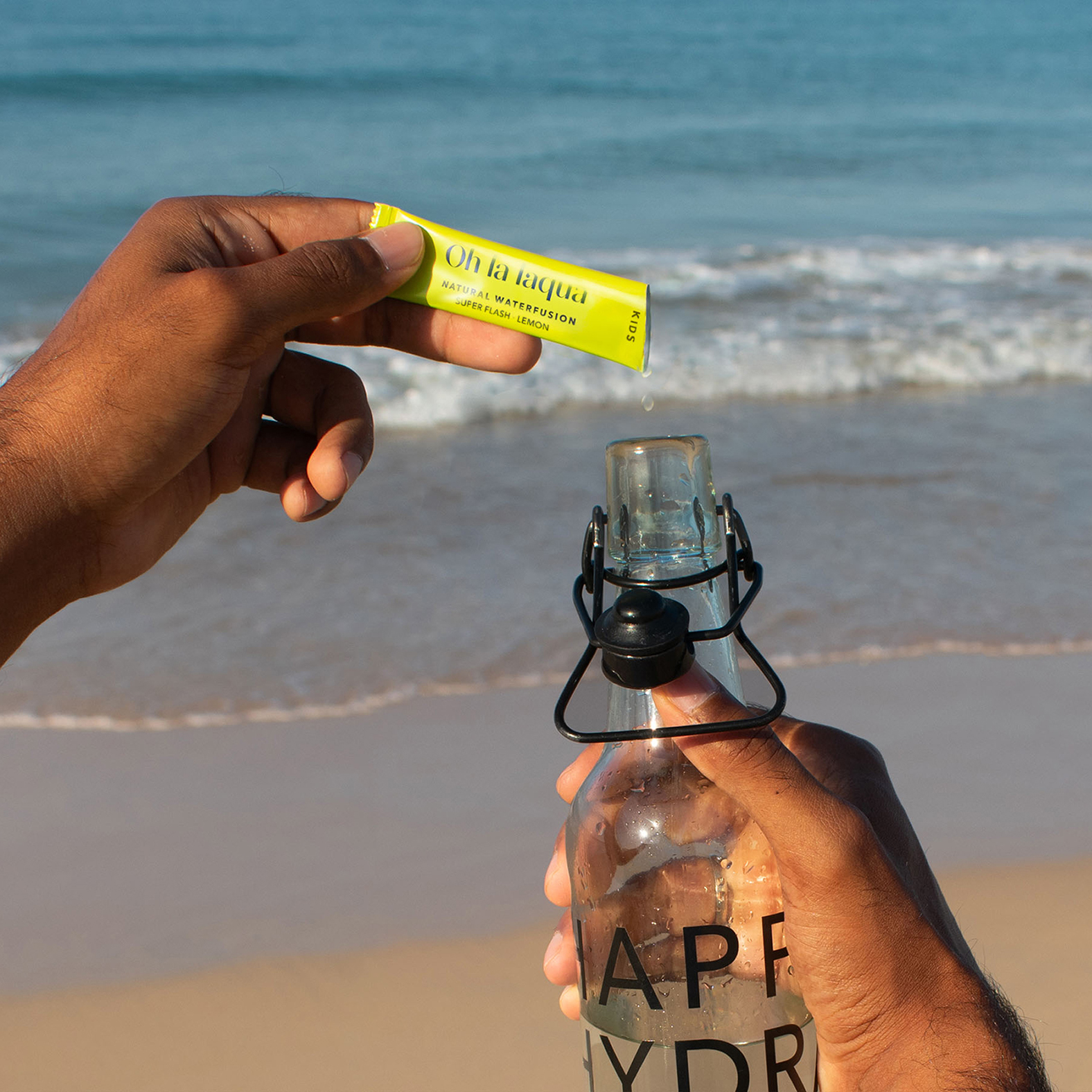 OHLALAQUA wird in eine Wasserflasche gegeben. Im Hintergrund ist ein Strand zu sehen.