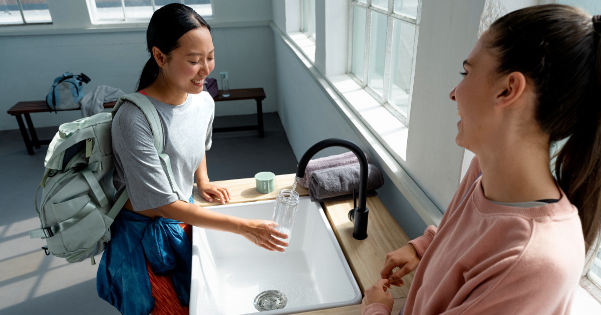 Zwei sportliche Frauen füllen am Wasserhahn Wasserfilterflasche auf
