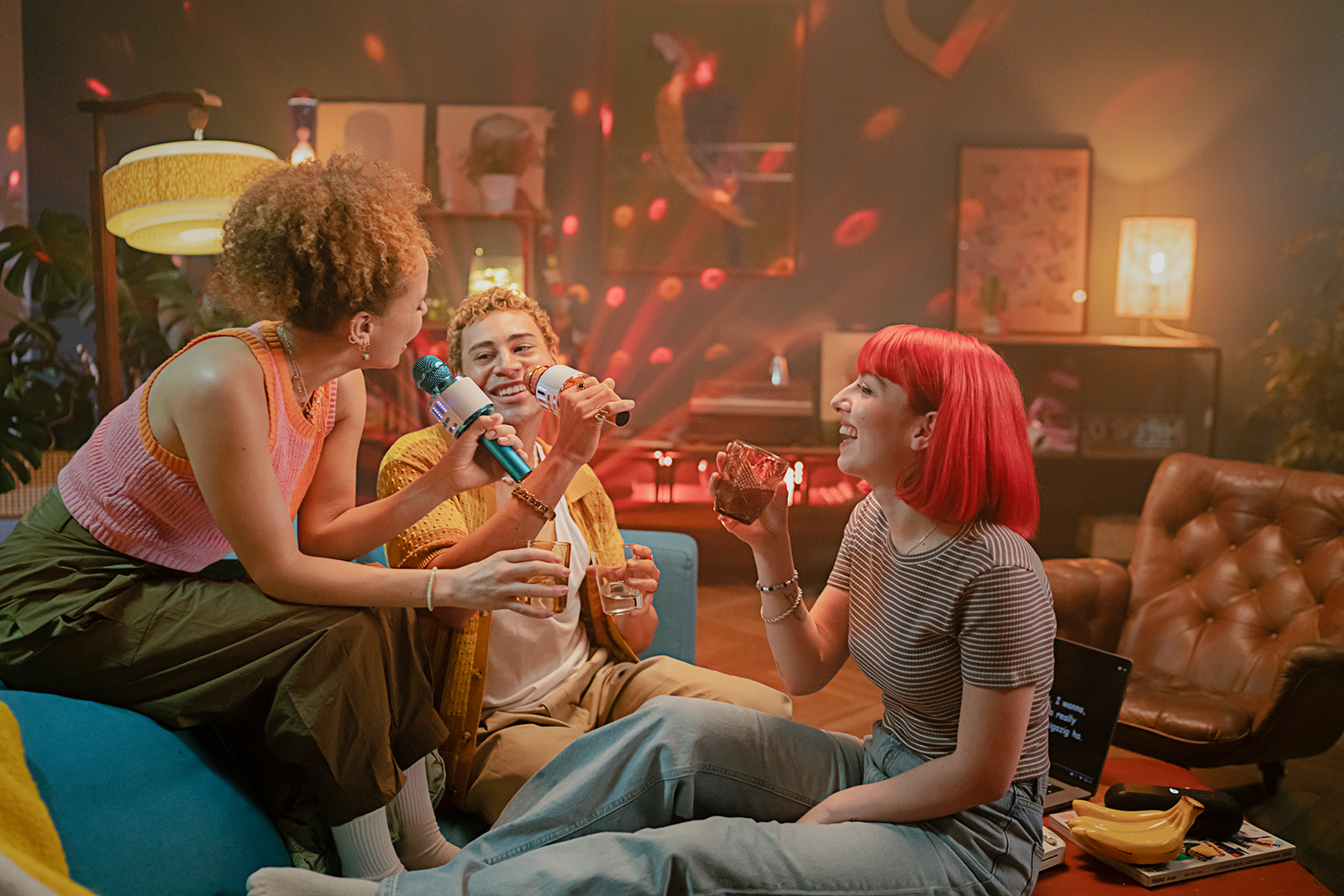 Drei Menschen singen Karaoke Drei Menschen singen in einem Wohnzimmer Karaoke. Eine rothaarige Frau trinkt Wasser.