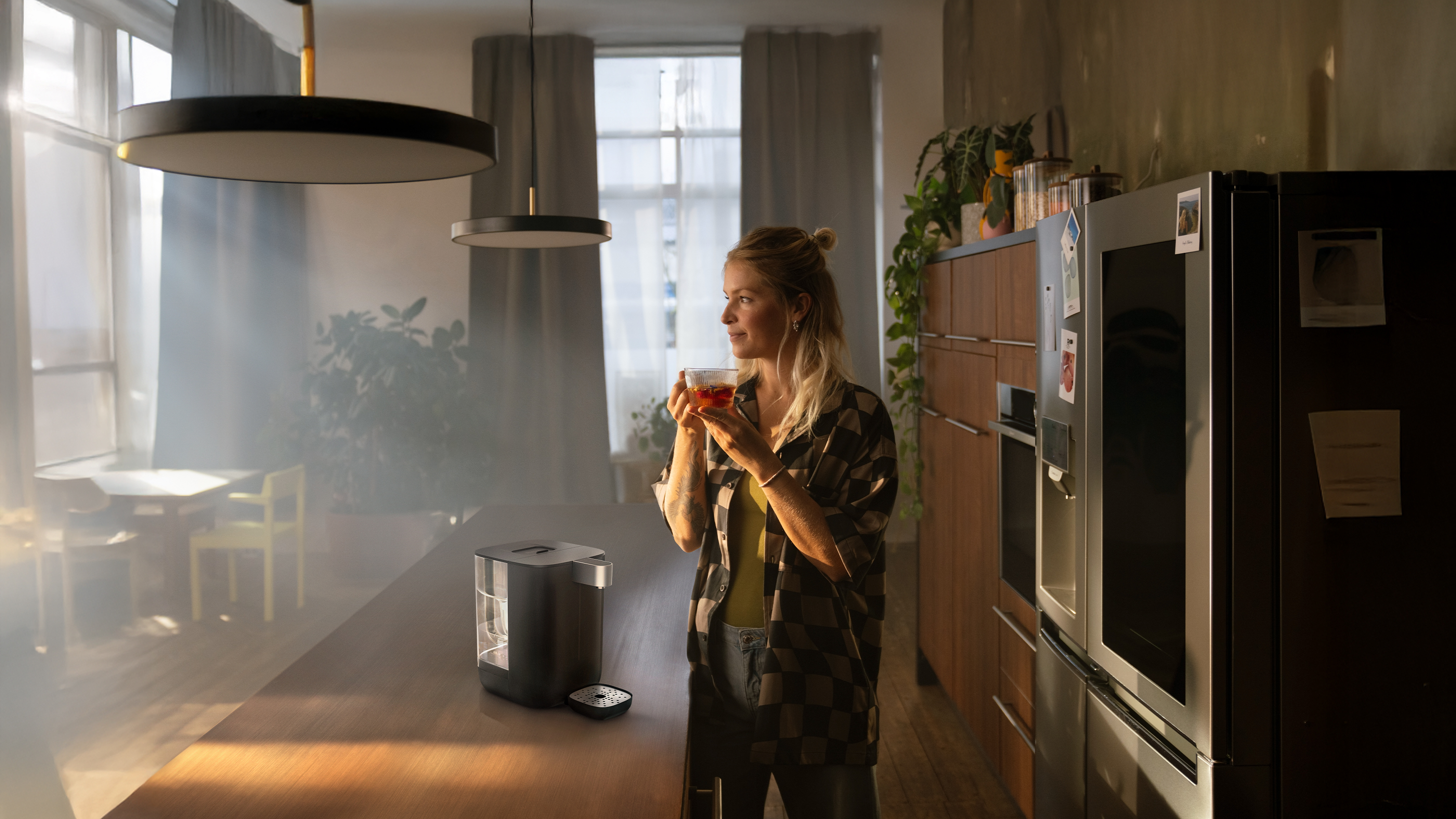 Eine Frau steht an die Küchentheke gelehnt neben dem BRITA Cube und trinkt eine Tasse Tee.