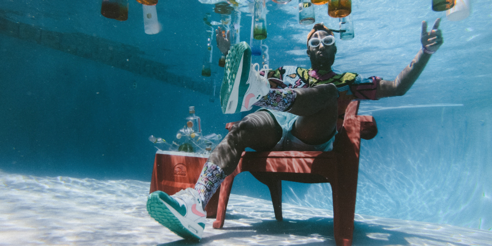 Mann sitzt unter Wasser in einem Pool, um in herum schweben Flaschen