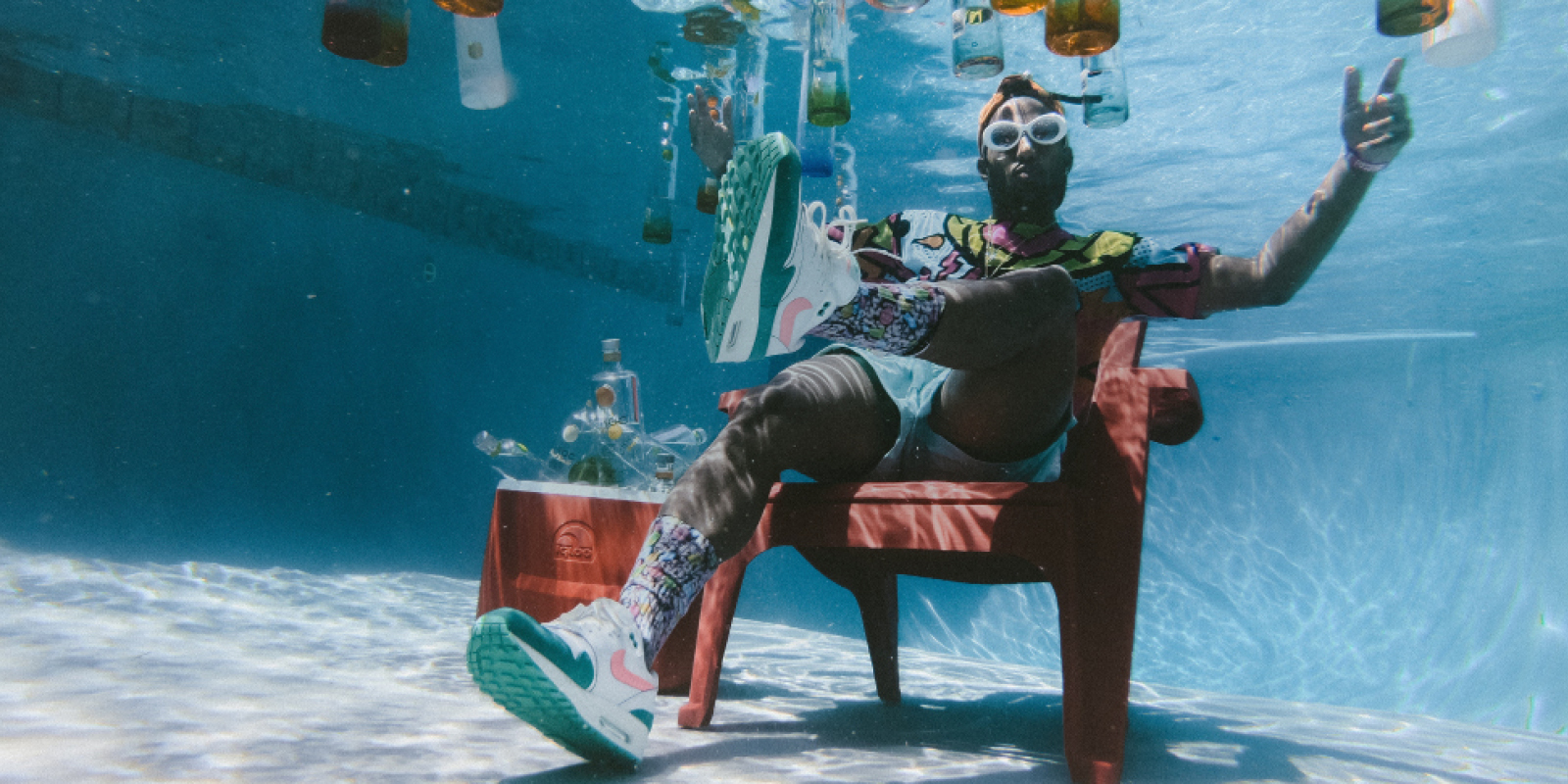 Mann sitzt unter Wasser Mann sitzt unter Wasser in einem Pool, um in herum schweben Flaschen