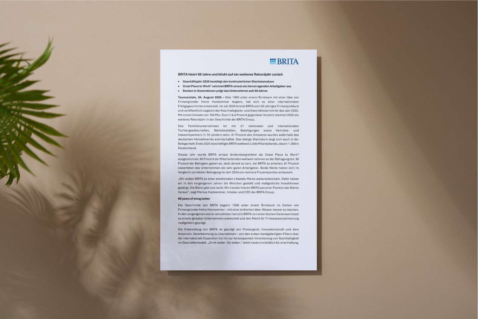 Dokument mit Pressemitteilung an einer Wand, links unscharfe Pflanze im Vordergrund.