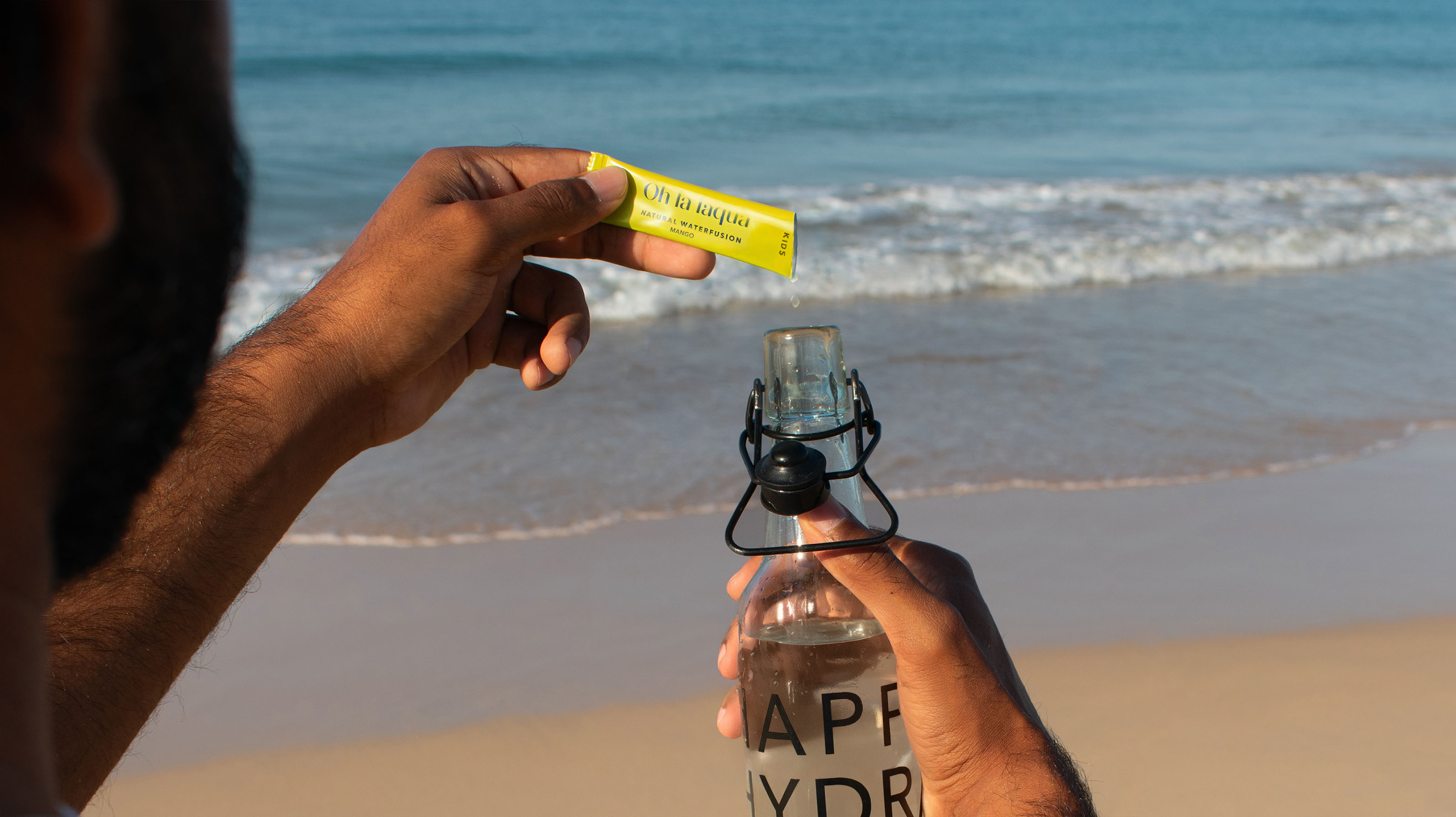 OHLALAQUA wird in eine Wasserflasche gegeben. Im Hintergrund ist ein Strand zu sehen.