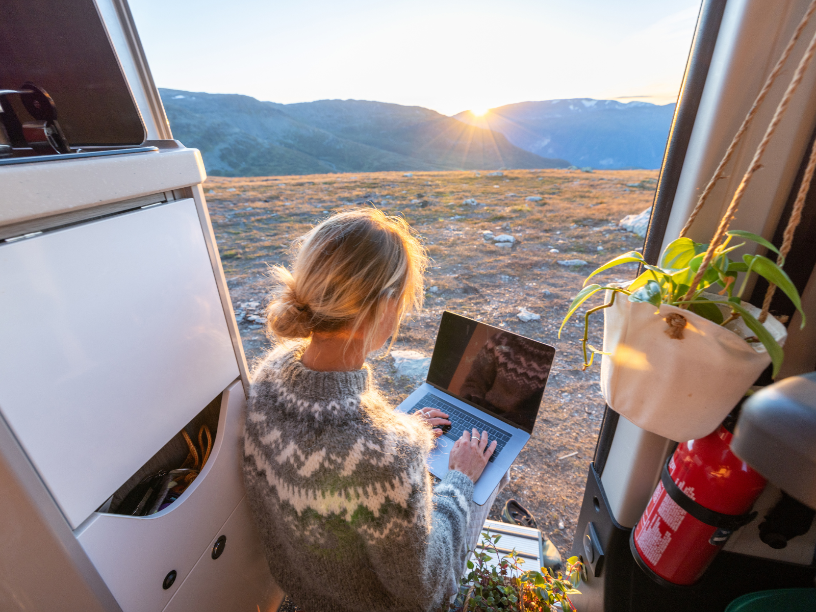 Gleichgewicht zwischen Arbeit und Freizeit: Frau sitzt mit Laptop im Camper in den Bergen.