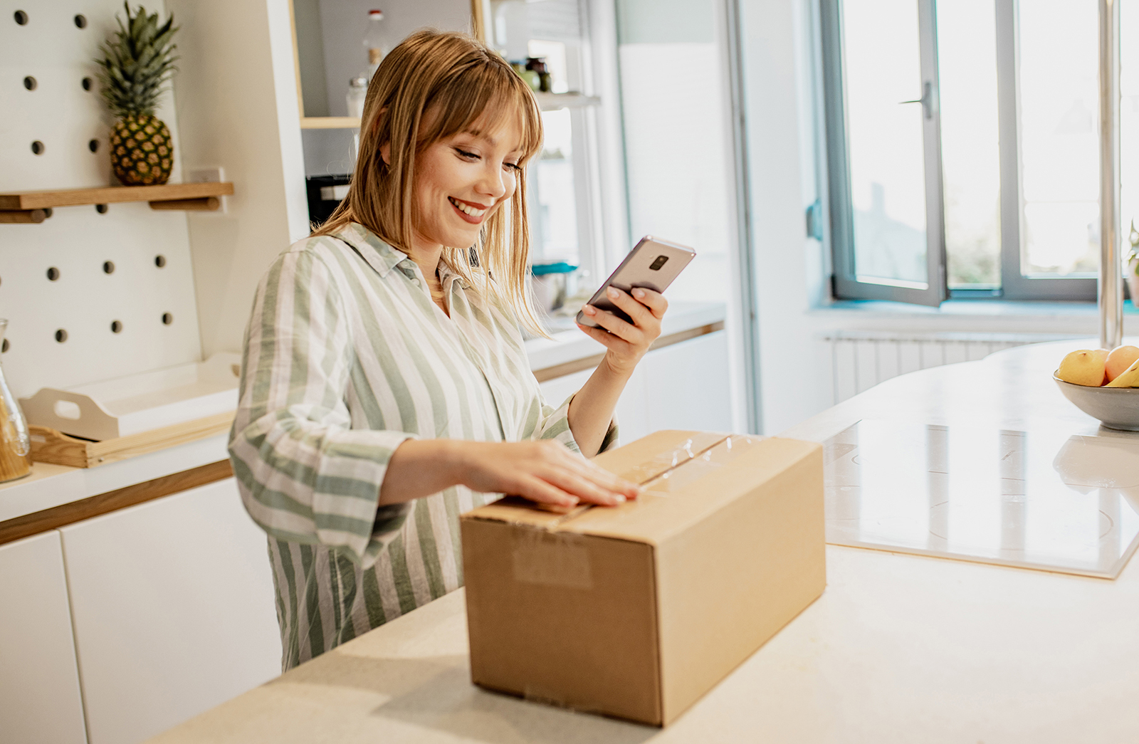 Eine Frau steht in der Küche und öffnet mit Vorfreude ein Paket