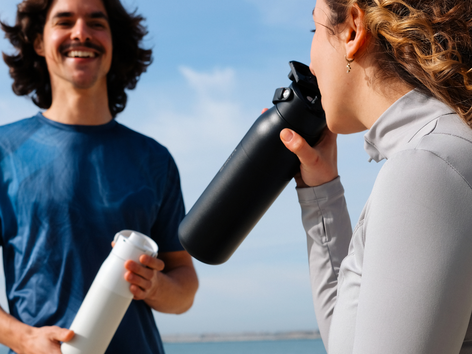 Zwei junge Personen machen eine Trinkpause zwischen ihrem Outdoor-Workout am Meer.