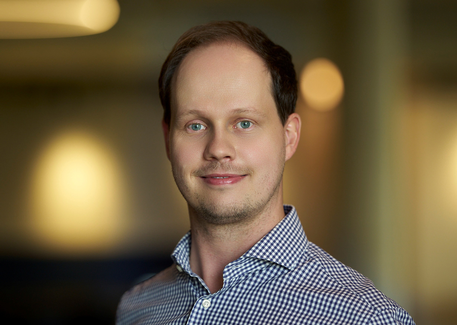 Porträtfoto von Maximilian Kranl, Pressekontakt bei BRITA Porträtfoto von Maximilian Kranl, Pressekontakt bei BRITA, vor warmem, unscharfem Bürohintergrund.
