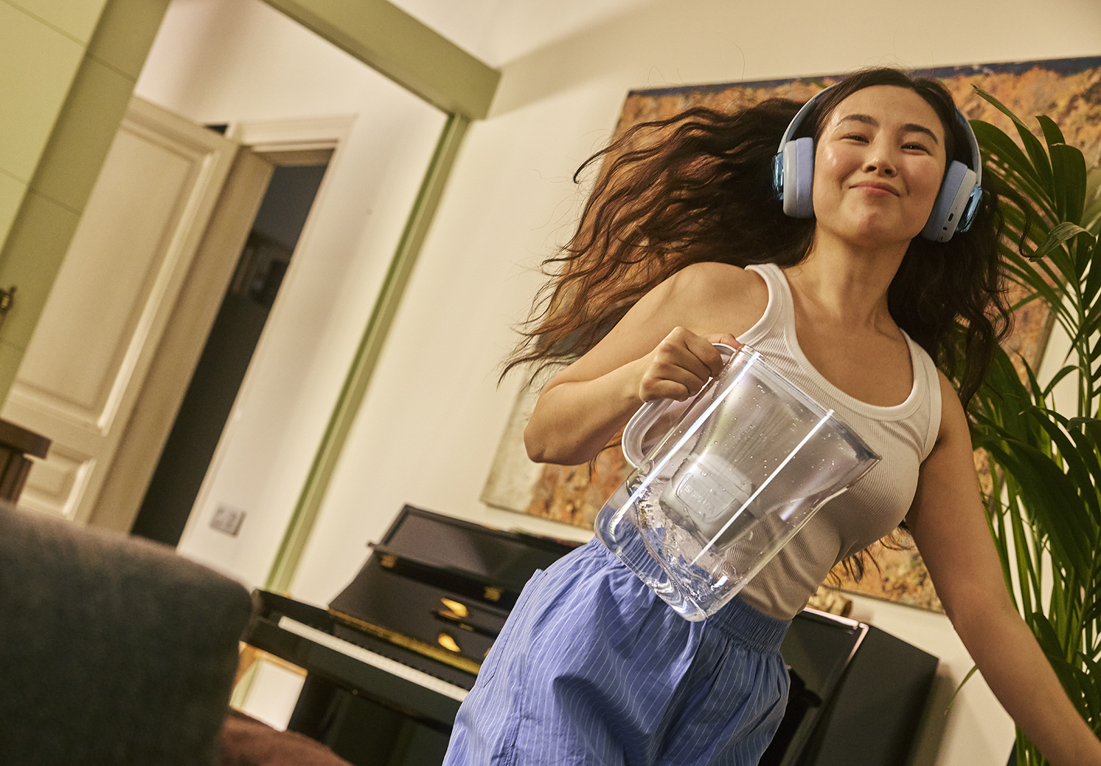Eine junge Frau tanzt glücklich zuhause mit dem Tischwasserfilter Style Essential in der Hand.
