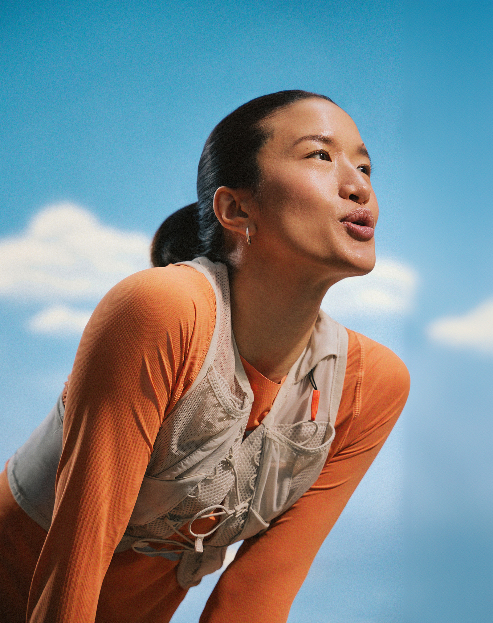 Läuferin in Sportkleidung mit Trinkweste lehnt sich leicht nach vorn, vor blauem Himmel