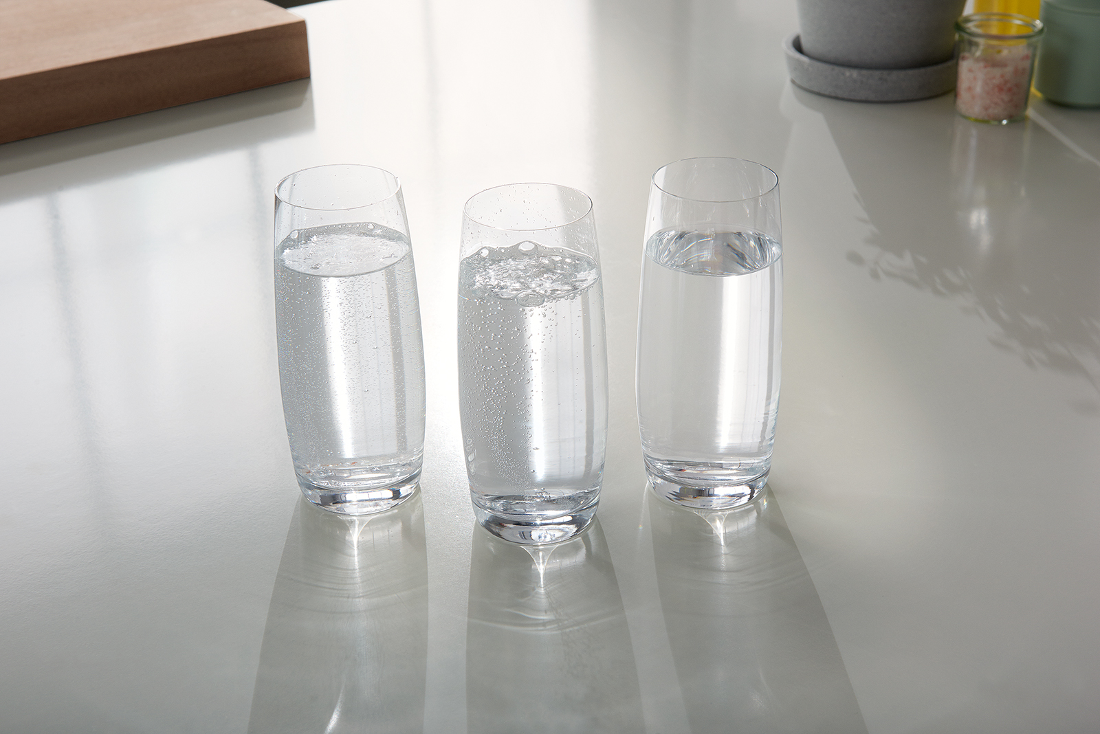 Drei gefüllte, durchsichtige Wassergläser mit unterschiedlich stark gesprudeltem Wasser. 