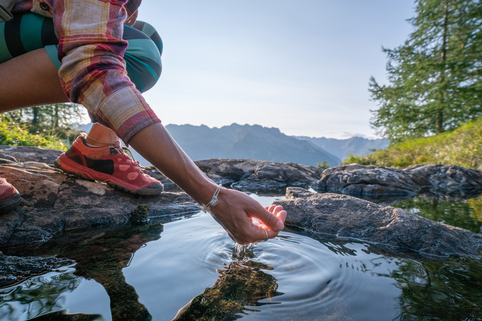 Jemand schöpft Wasser in den Bergen mit der Hand Eine Hand taucht in einen Wasserlauf in den Bergen