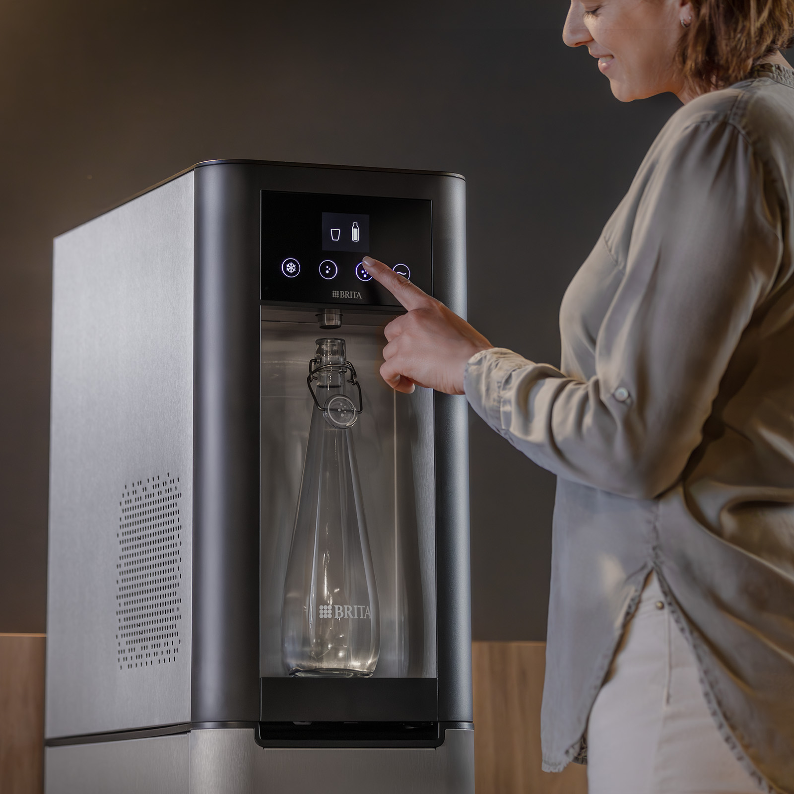Frau füllt ein Glas Wasser am Dispenser auf Eine blonde Frau benutzt den Wasserspender top pro, um sich ein Glas Wasser einzuschenken.