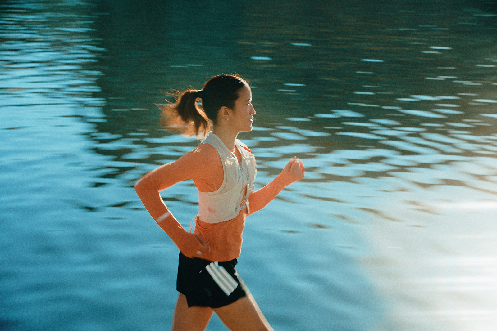 Läuferin in Sportkleidung joggt am Wasser entlang, mit reflektierender Wasseroberfläche
