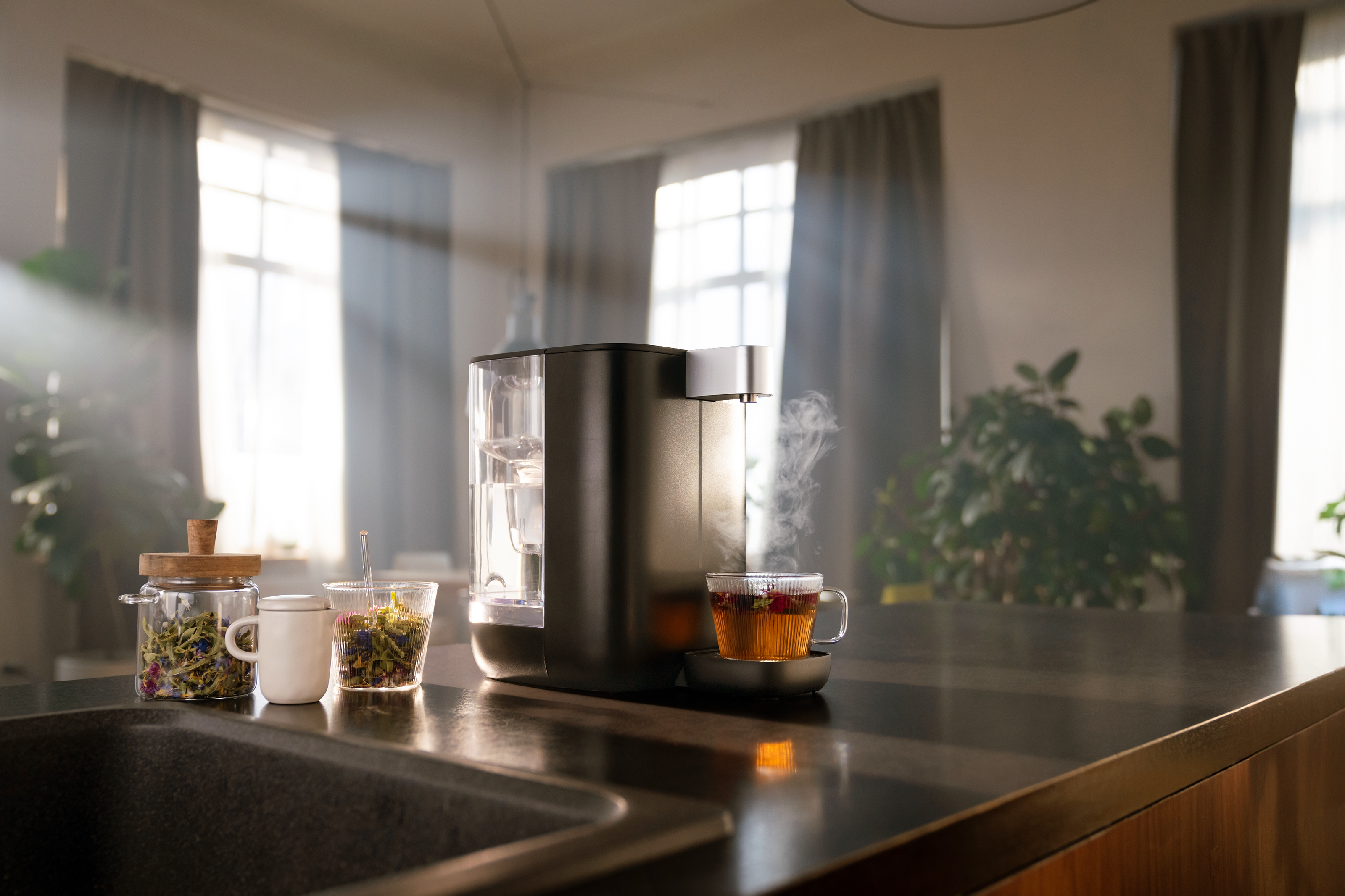 BRITA Cube steht mit Teetasse auf Theke Ein schwarzer BRITA Cube steht neben einer Spüle. Eine dampfende Tasse Tee steht vor dem Heißwassers
