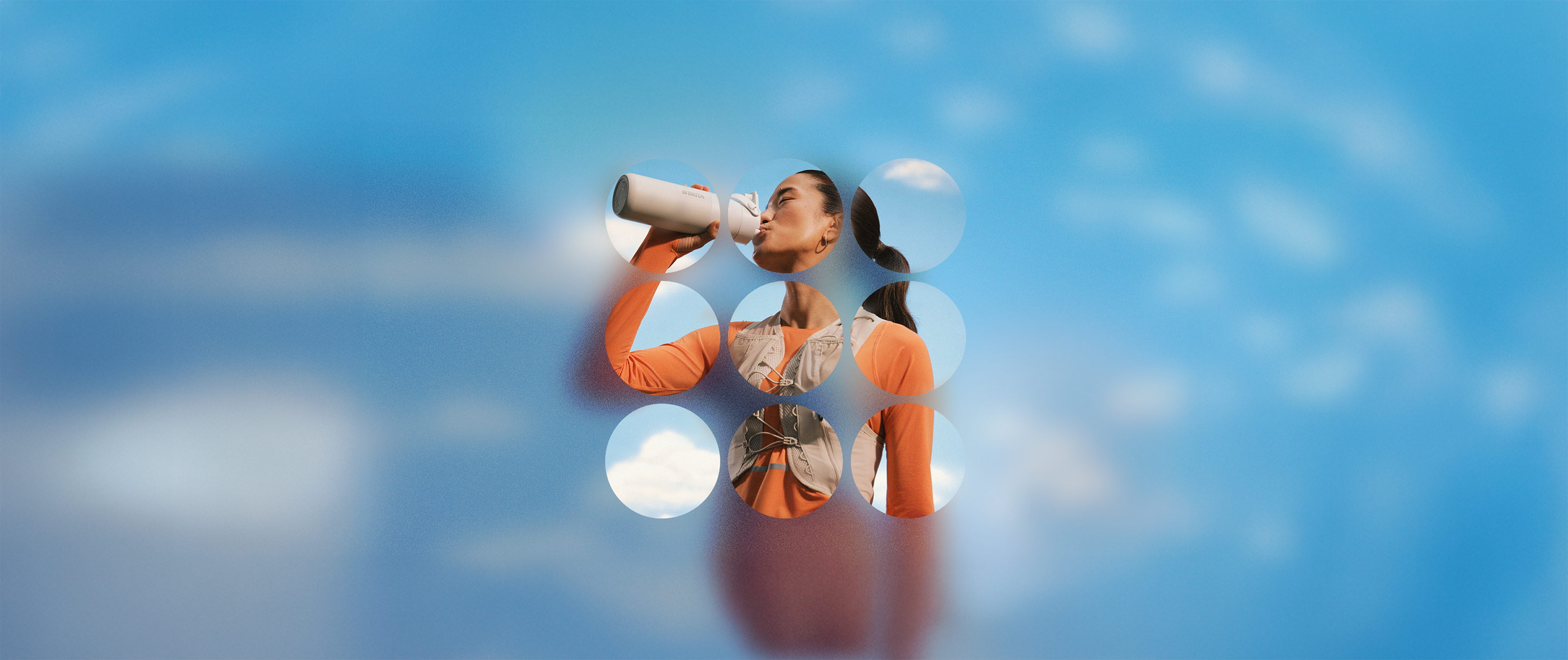 Läuferin in Sportkleidung trinkt aus einer Trinkflasche, vor blauem Himmel