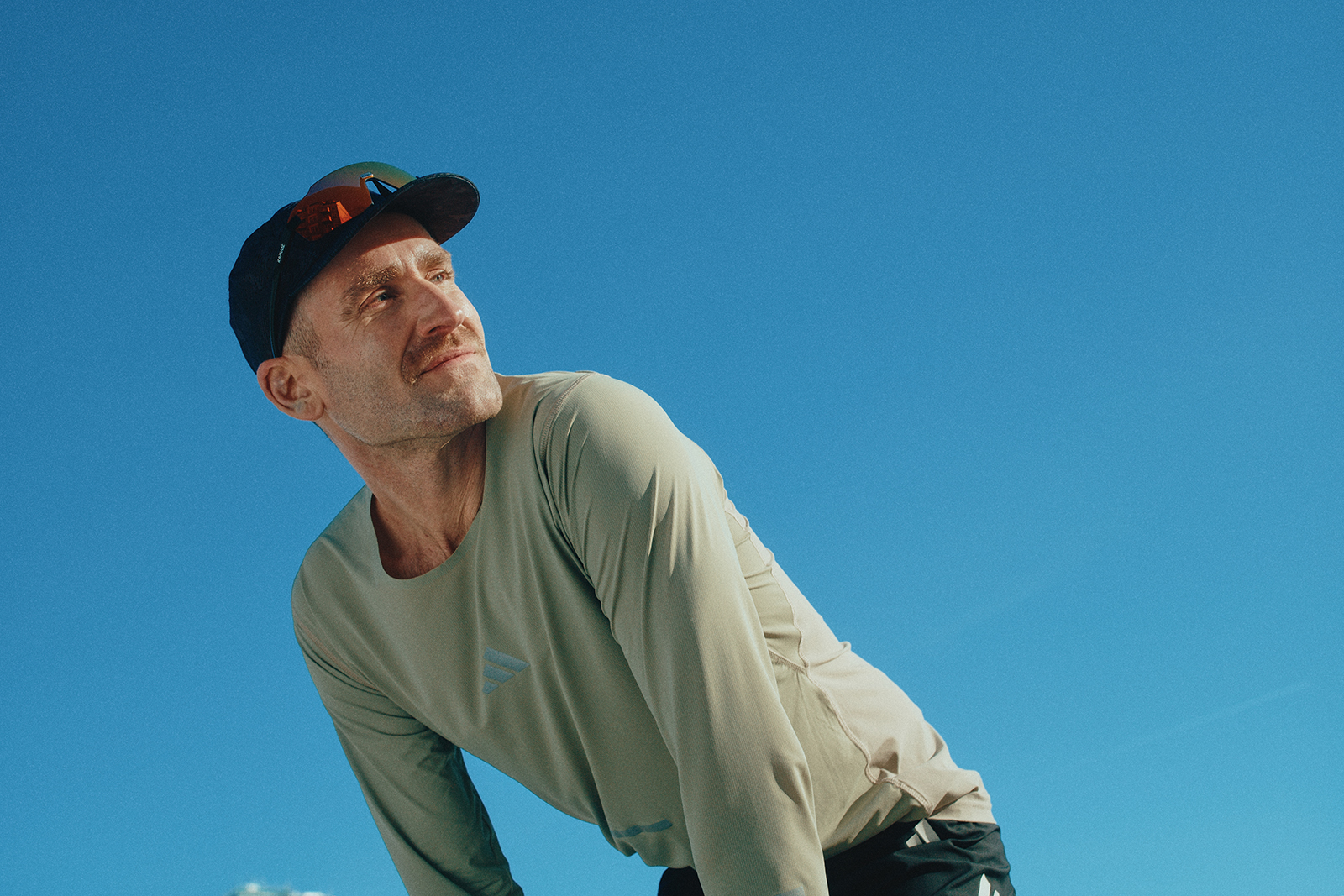 Sportlicher Läufer in Funktionskleidung lehnt sich leicht nach vorn vor klarem, blauem Himmel