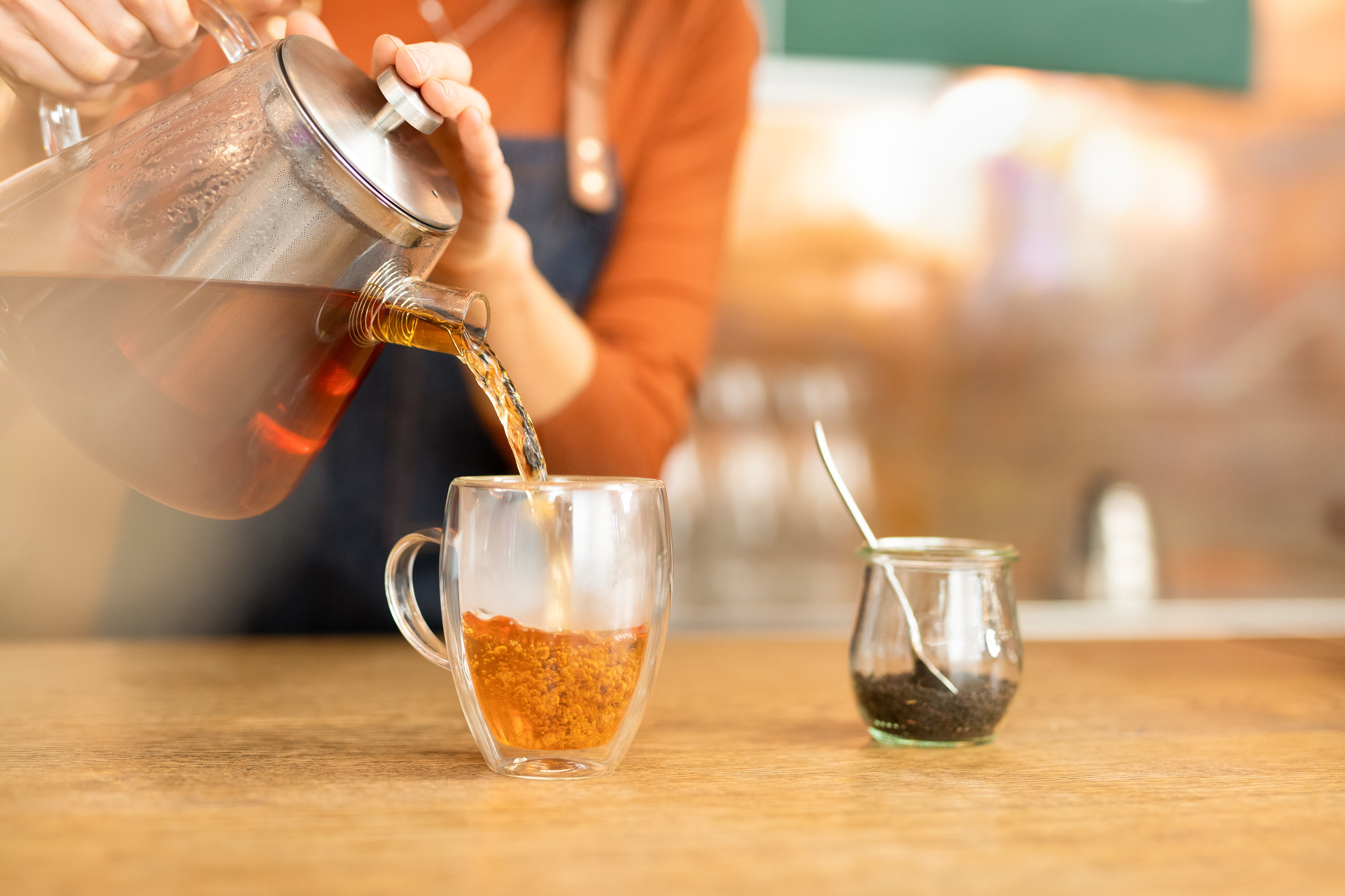 Tee wird in ein Teeglas gefüllt Tee wird aus einer Teekanne aus Glas in ein Teeglas gefüllt